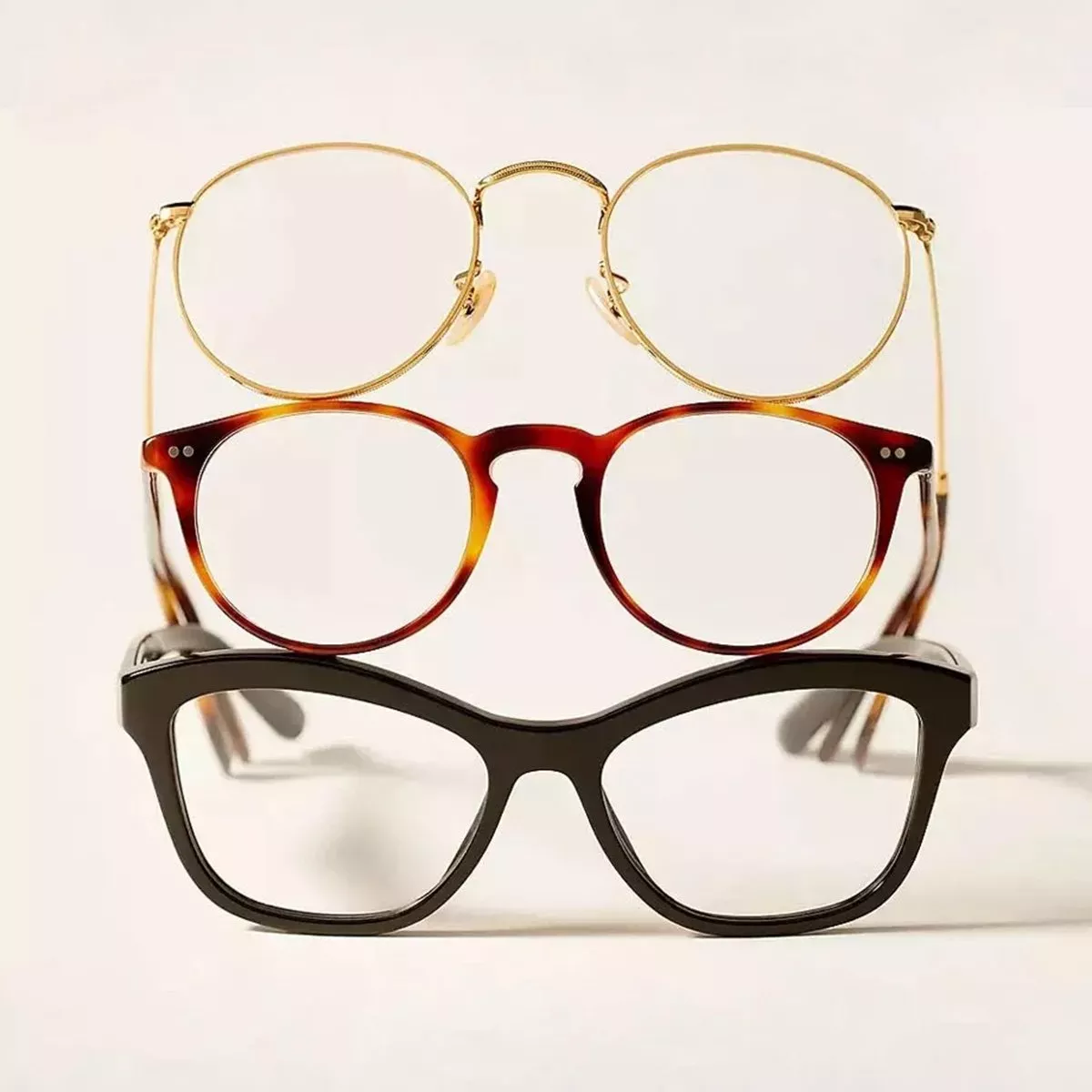 three pairs of eyeglasses stacked vertically, showcasing different frame styles: round gold wire-rimmed, round tortoiseshell acetate, and thick black square/cateye