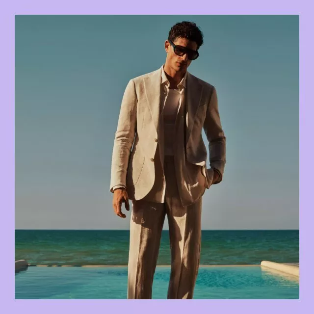 Stylish man in beige linen suit and sunglasses by pool with sea backdrop, summer menswear fashion shoot