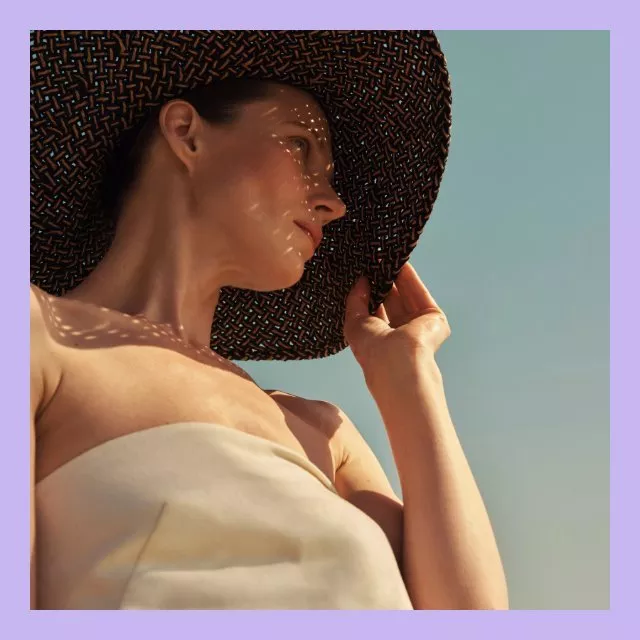 Woman in wide-brim straw sun hat and strapless dress, summer fashion portrait against clear blue sky