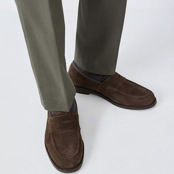 A close-up shot of a man's feet in brown suede loafers and green trousers.