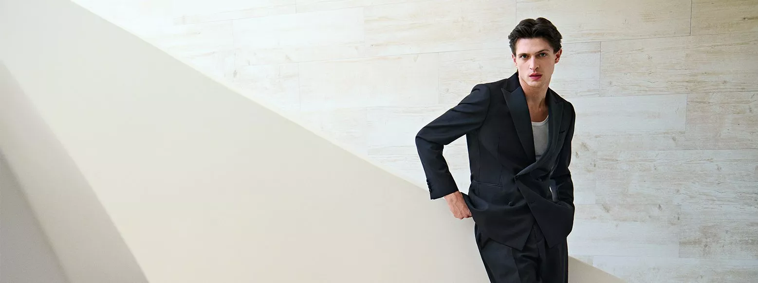 Male model in black tailored suit by pale stone wall, modern fashion portrait with clean architectural lines