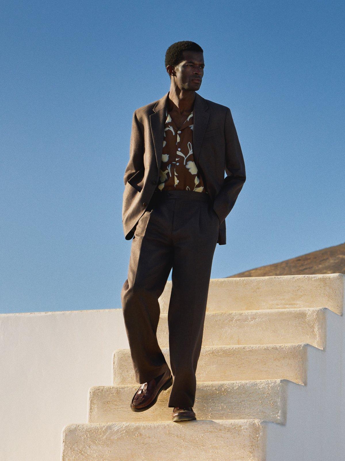 a model wearing a bold shirt with a brown suit jacket on walking down some white steps