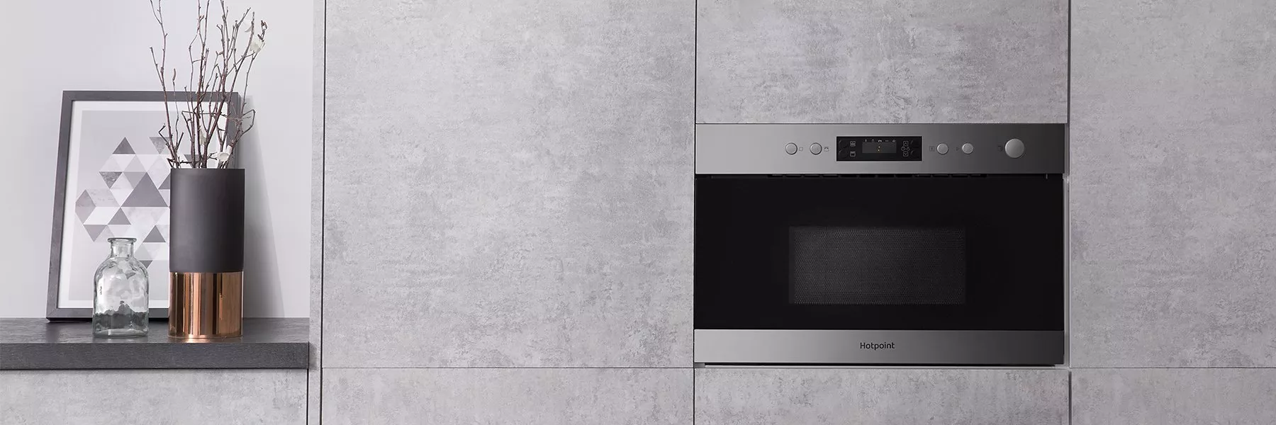 Modern built-in stainless steel Hotpoint microwave oven in grey concrete kitchen units with minimalist decor