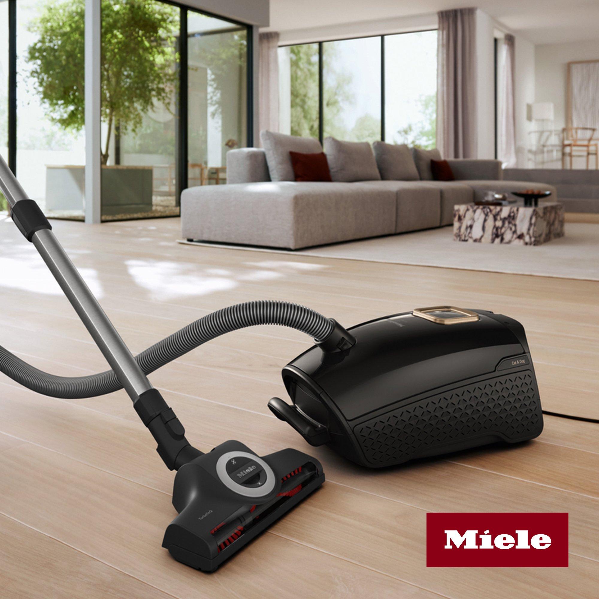Miele vacuum cleaner in a modern, bright living room with wooden flooring and a sectional sofa