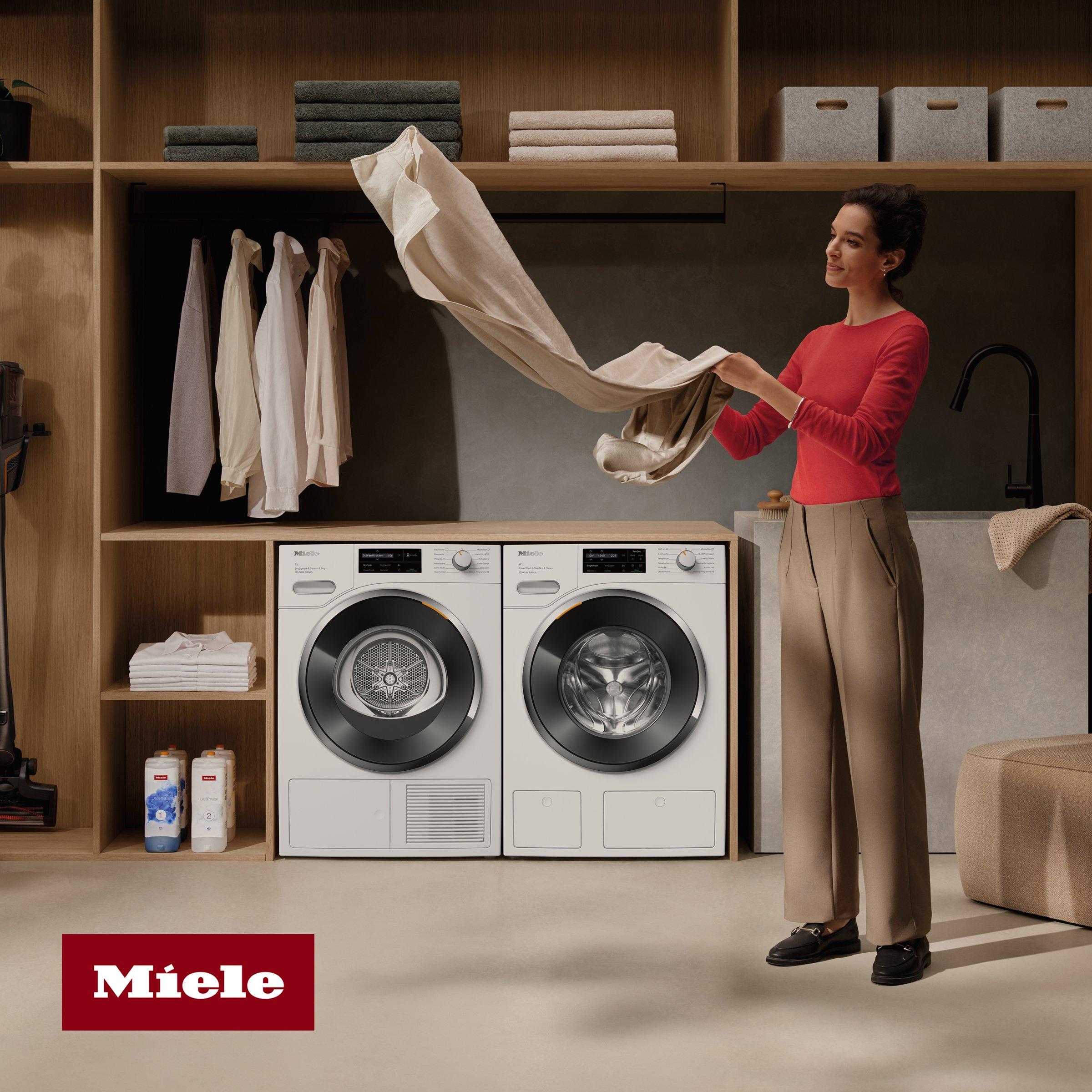 A woman folding laundry in a modern, organized laundry room featuring Miele washer and dryer appliances