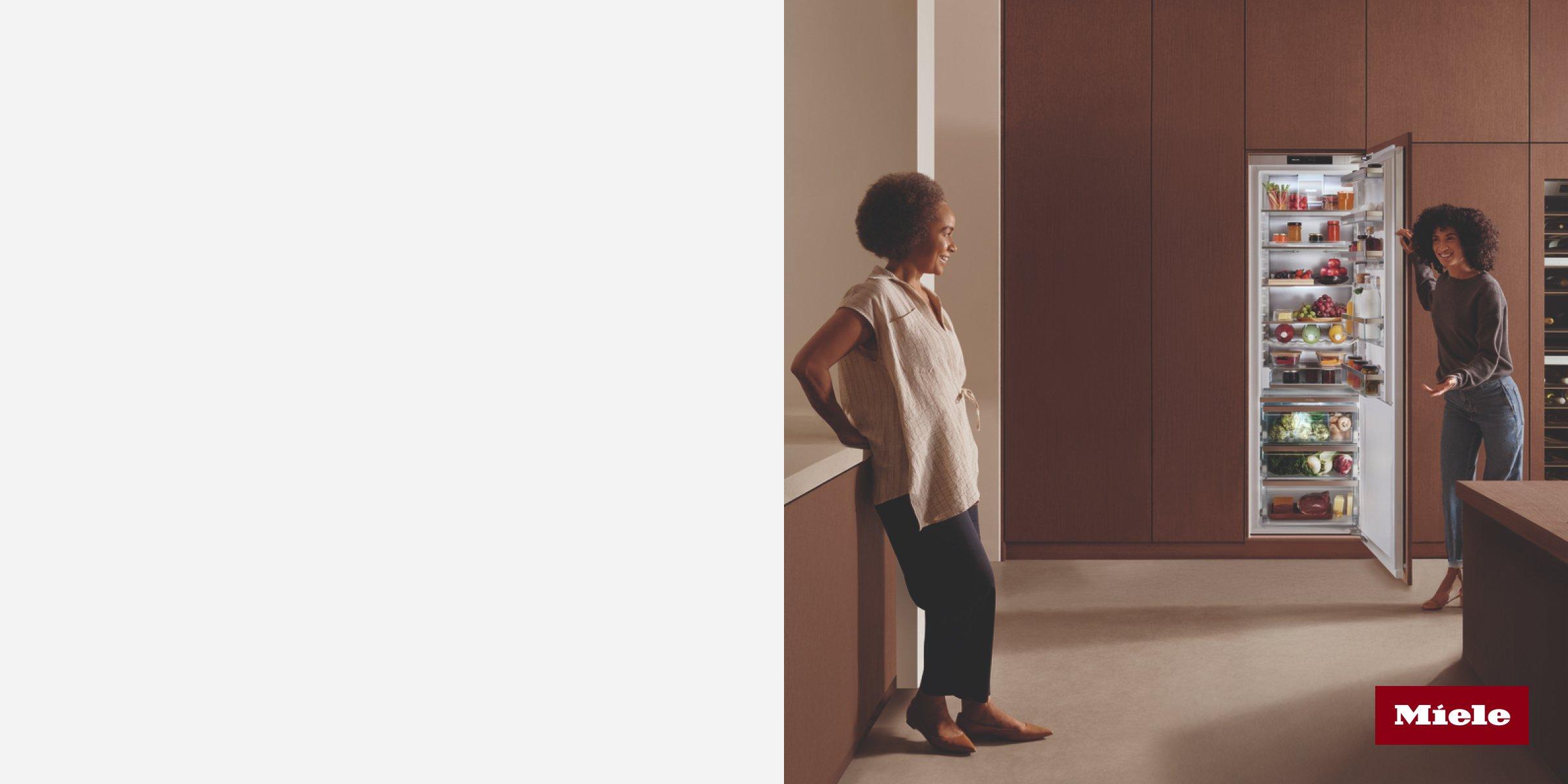 Two women interacting with a Miele refrigerator and wine cooler.