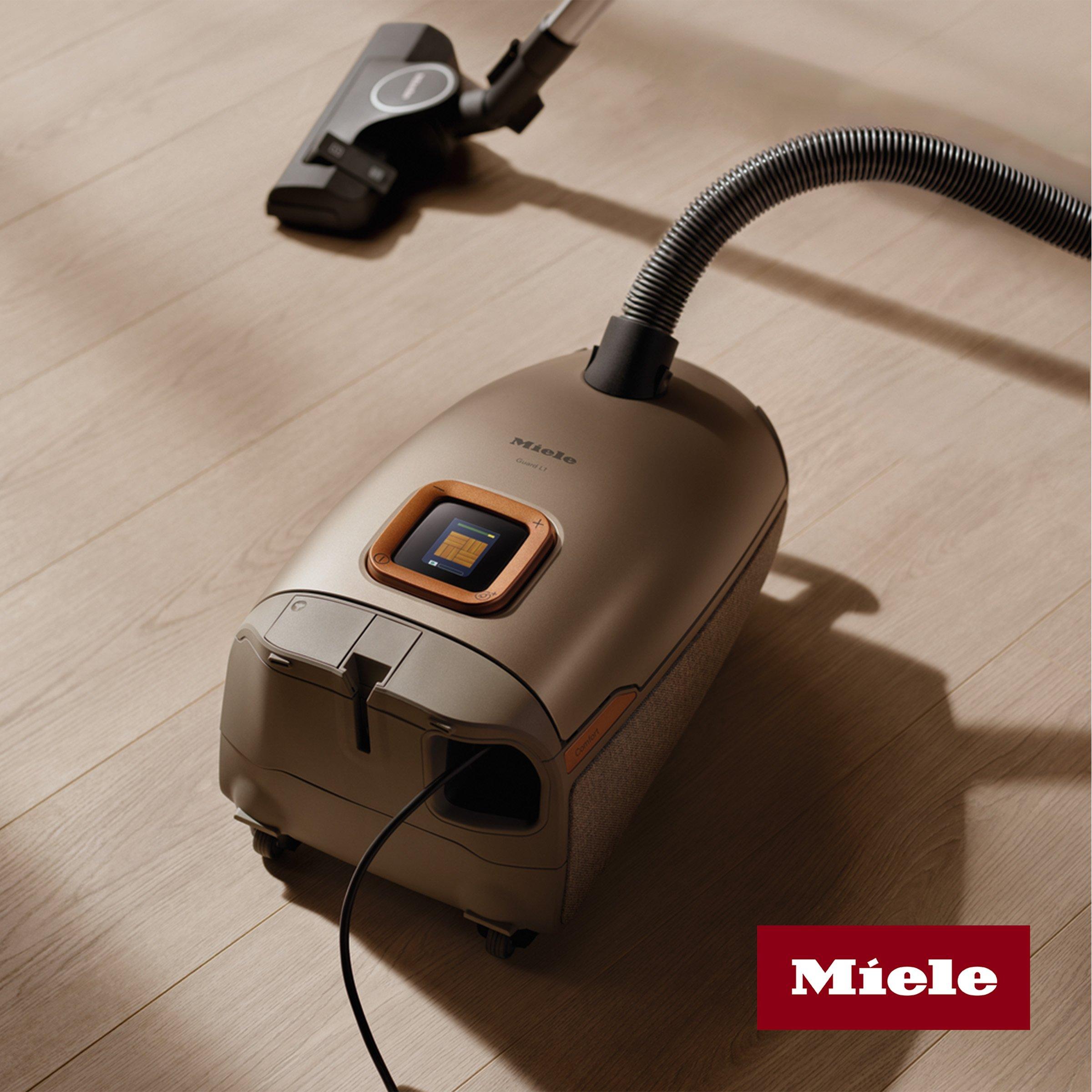 A Miele vacuum cleaner with a sleek design and digital display is shown on a wooden floor