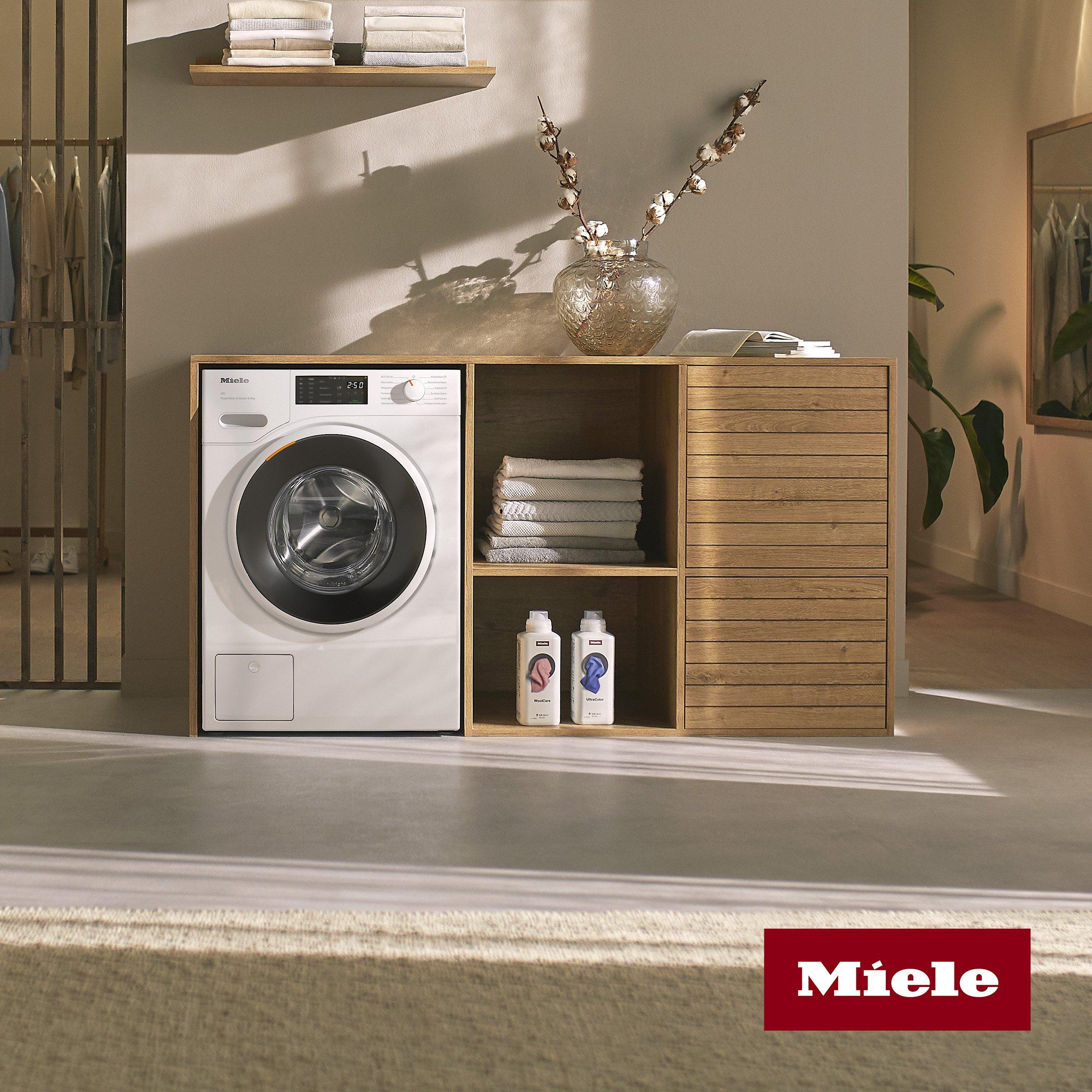 miele washing machine on the floor in the cabinet with towel and detergent