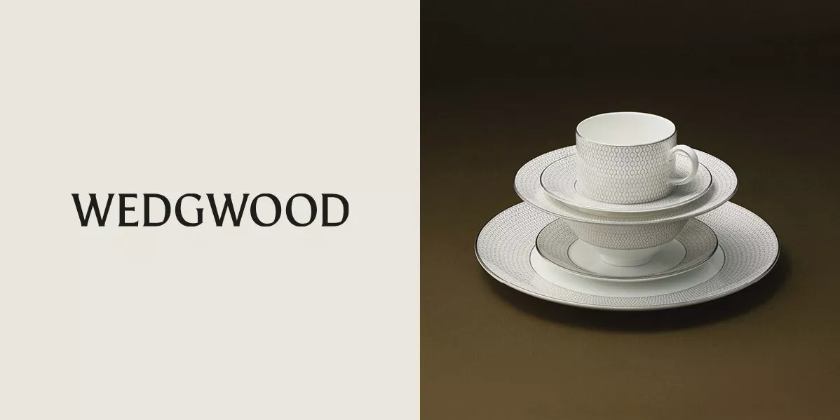 Logo for Wedgwood on the left and a stacked set of its white fine bone china featuring a grey geometric honeycomb pattern and platinum rim on the right, against a dark brown background.