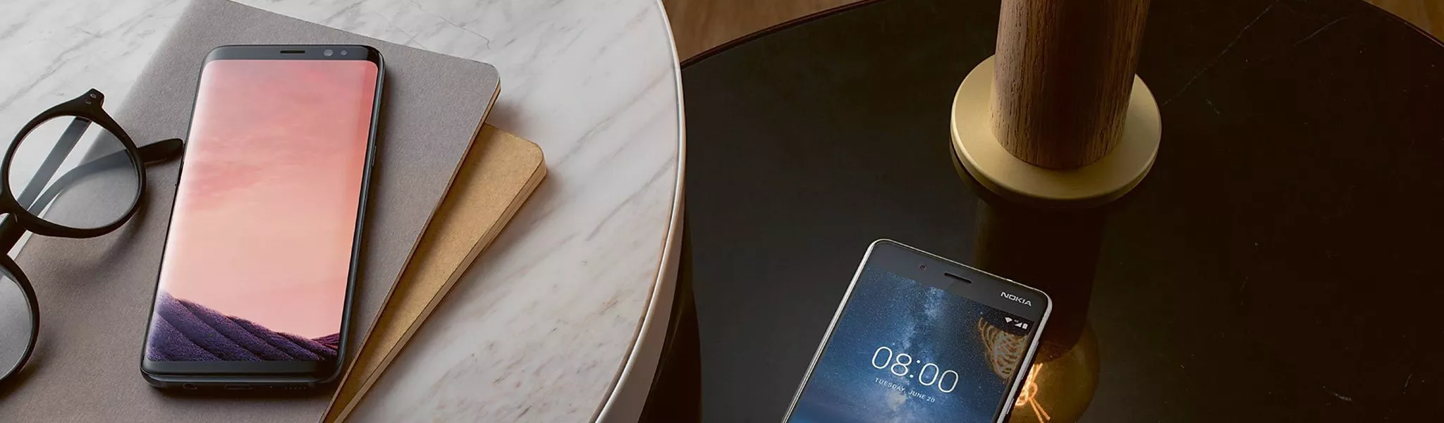 Two smartphones on a marble and glass table beside notebooks and glasses, modern mobile tech flat lay scene