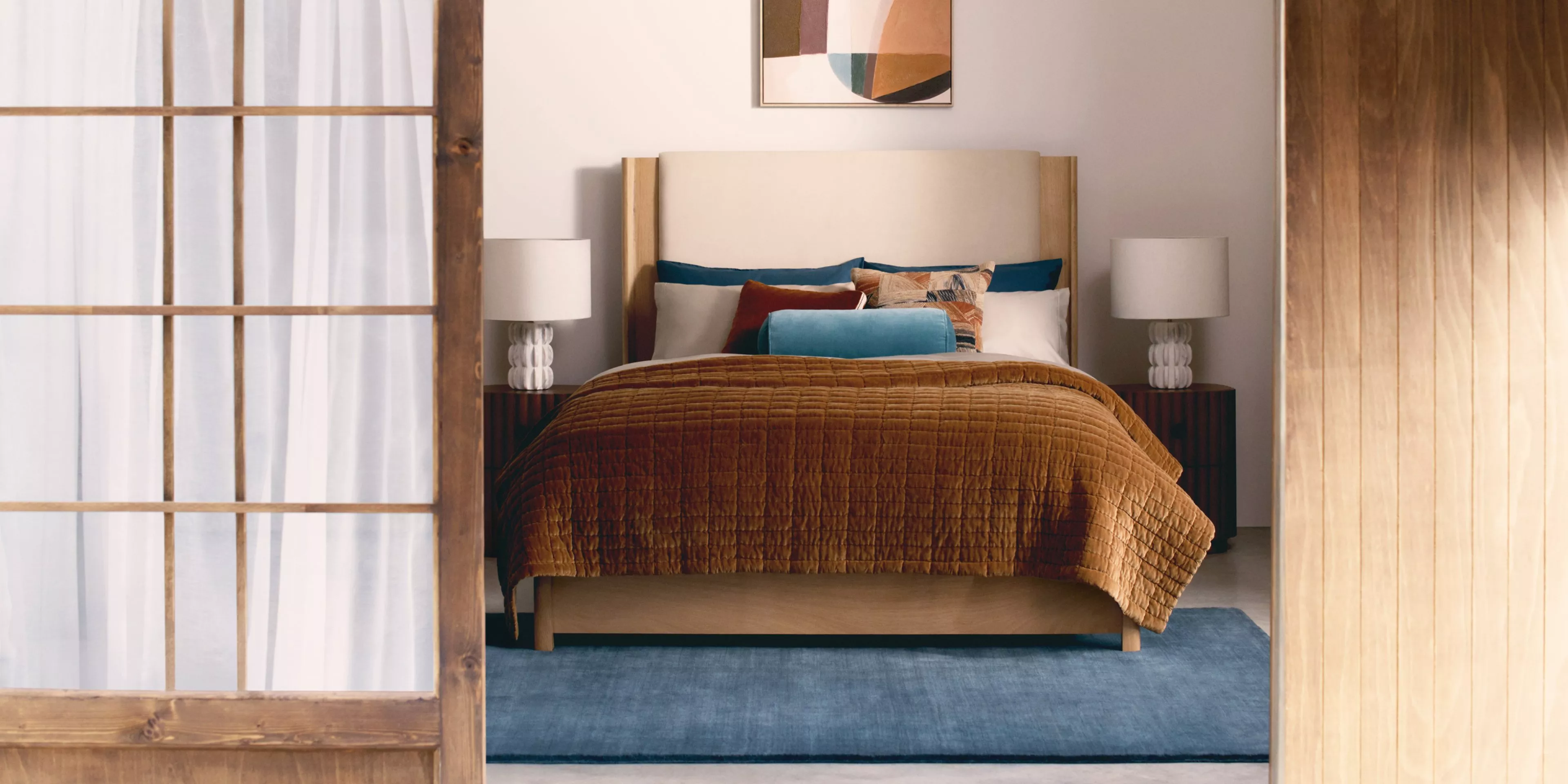 Stylish bedroom with abstract art, cosy bedding, and a modern lamp. Warm tones create a serene atmosphere.