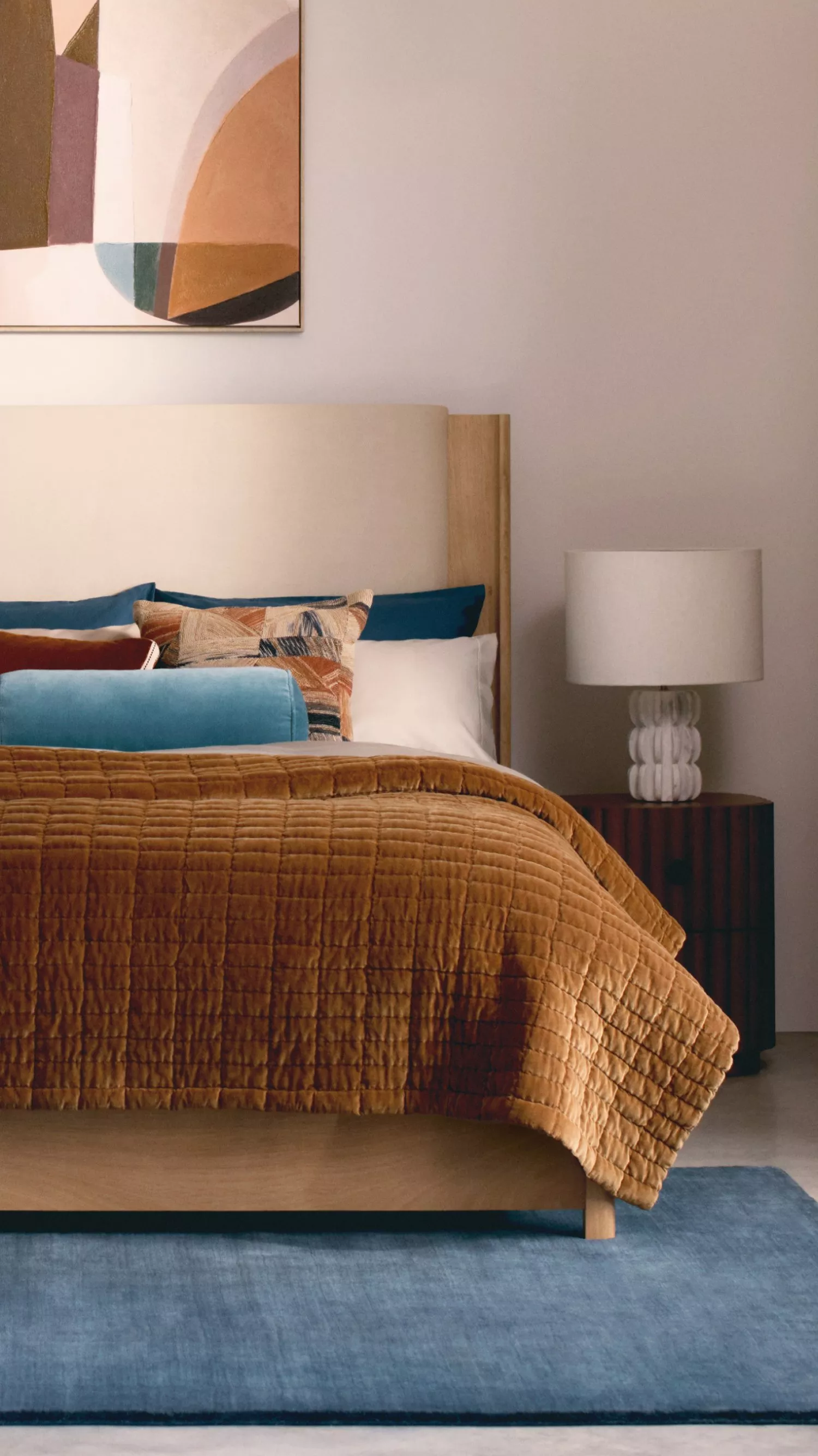 Stylish bedroom with abstract art, cosy bedding, and a modern lamp. Warm tones create a serene atmosphere.