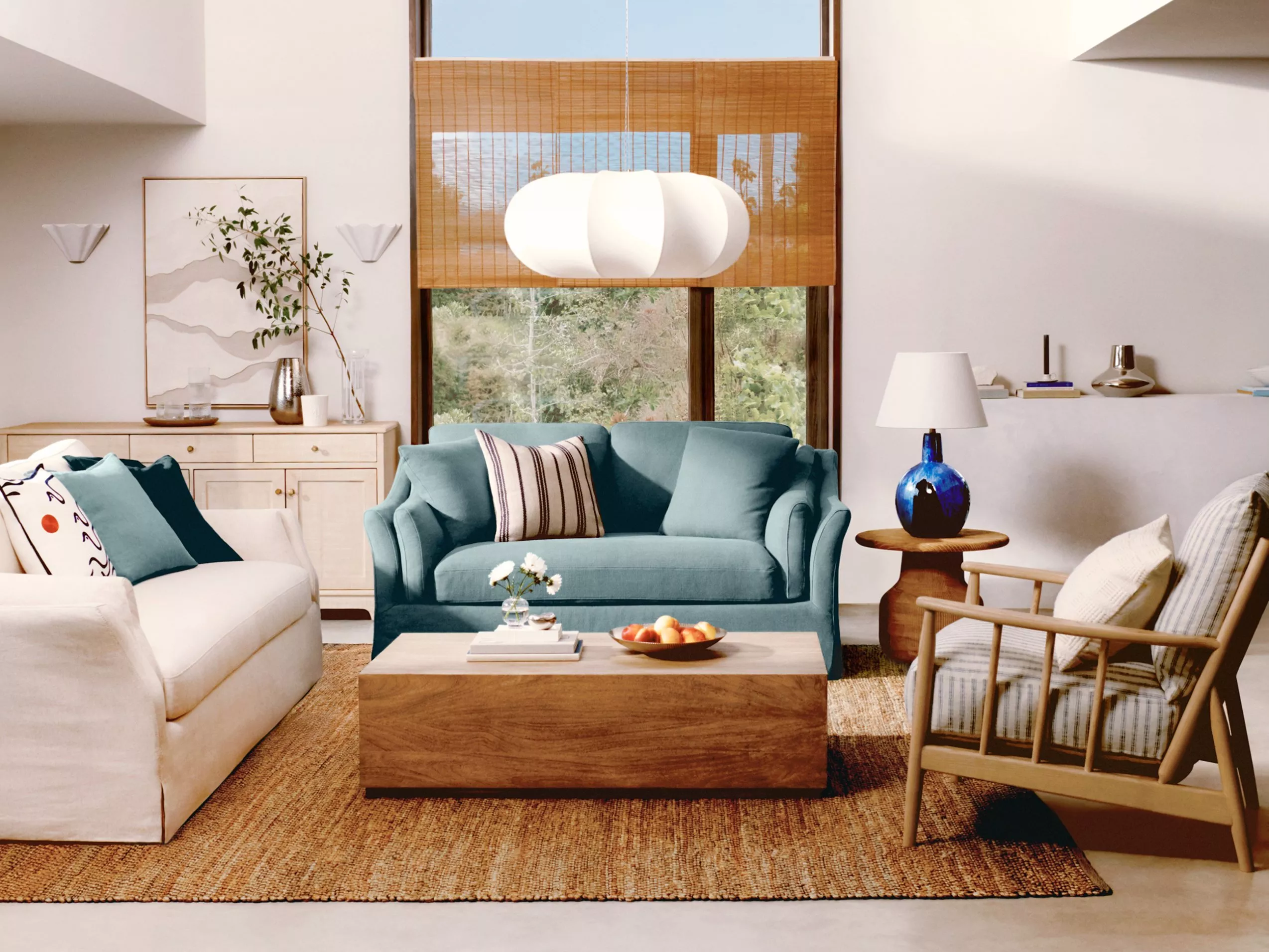 Stylish living room with a teal sofa, modern decor, and wooden accents. Large window offers a scenic view.