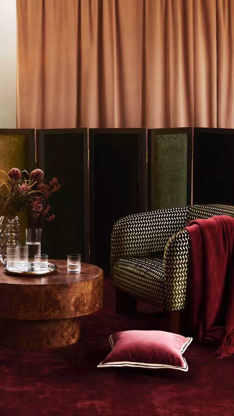 Luxury living room with patterned armchair, burgundy throw, round wood coffee table and velvet curtains backdrop