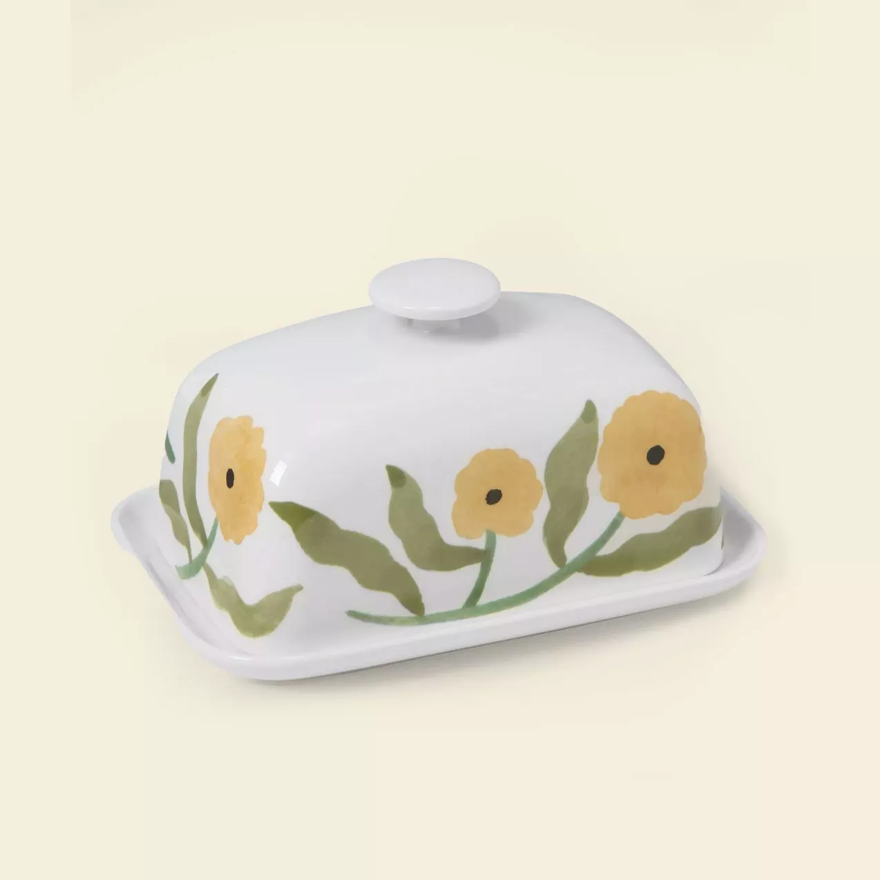 White ceramic butter dish with yellow floral design and green leaves on a soft beige background.