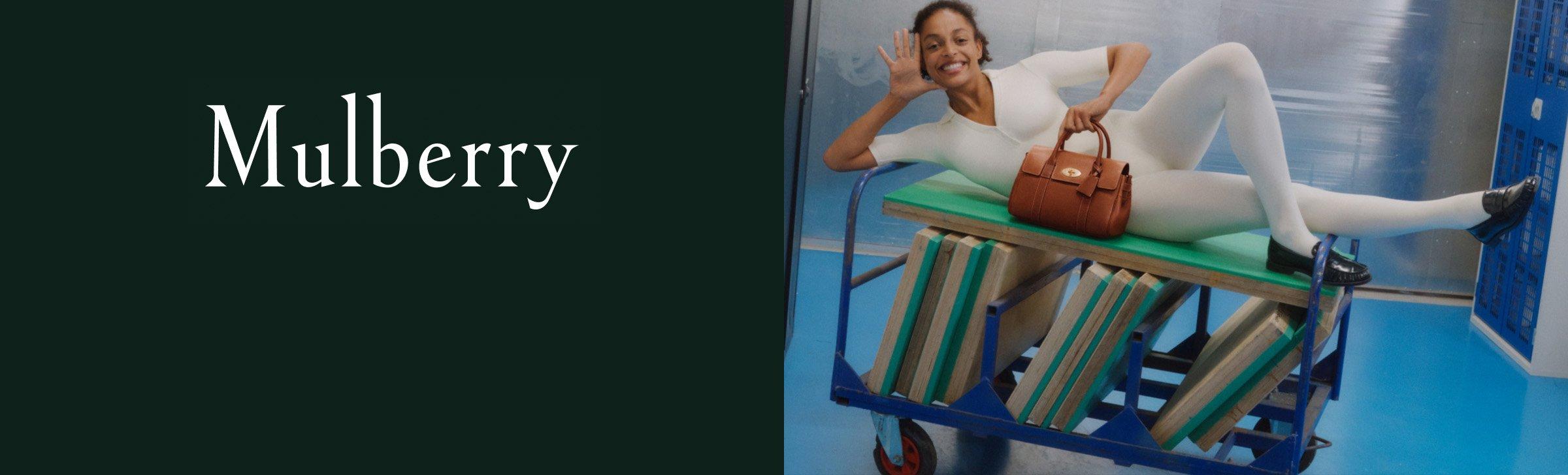 Model in white bodysuit posing on a cart with a brown Mulberry handbag