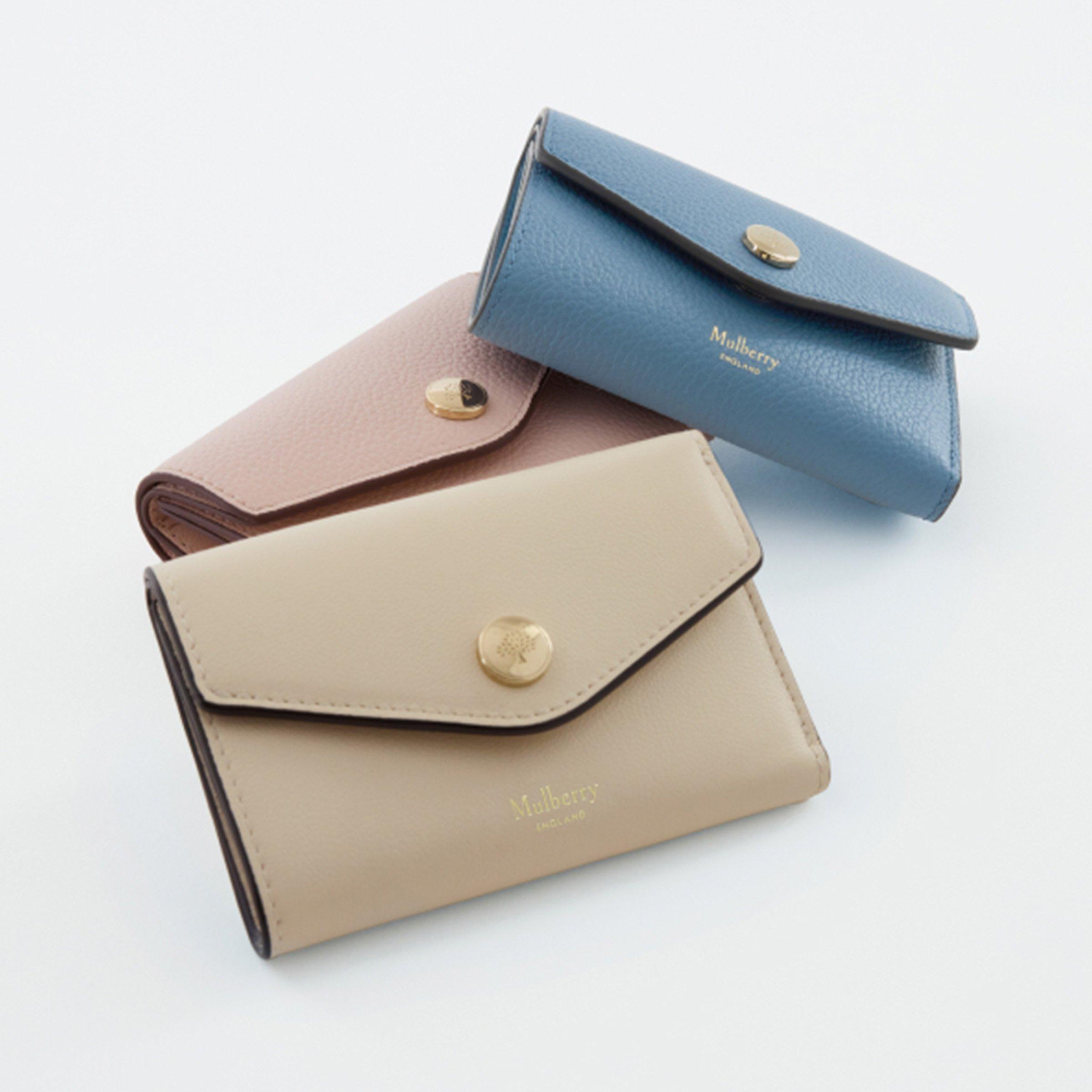 Three elegant Mulberry wallets in beige, pink, and blue leather with gold button clasps displayed on a white background