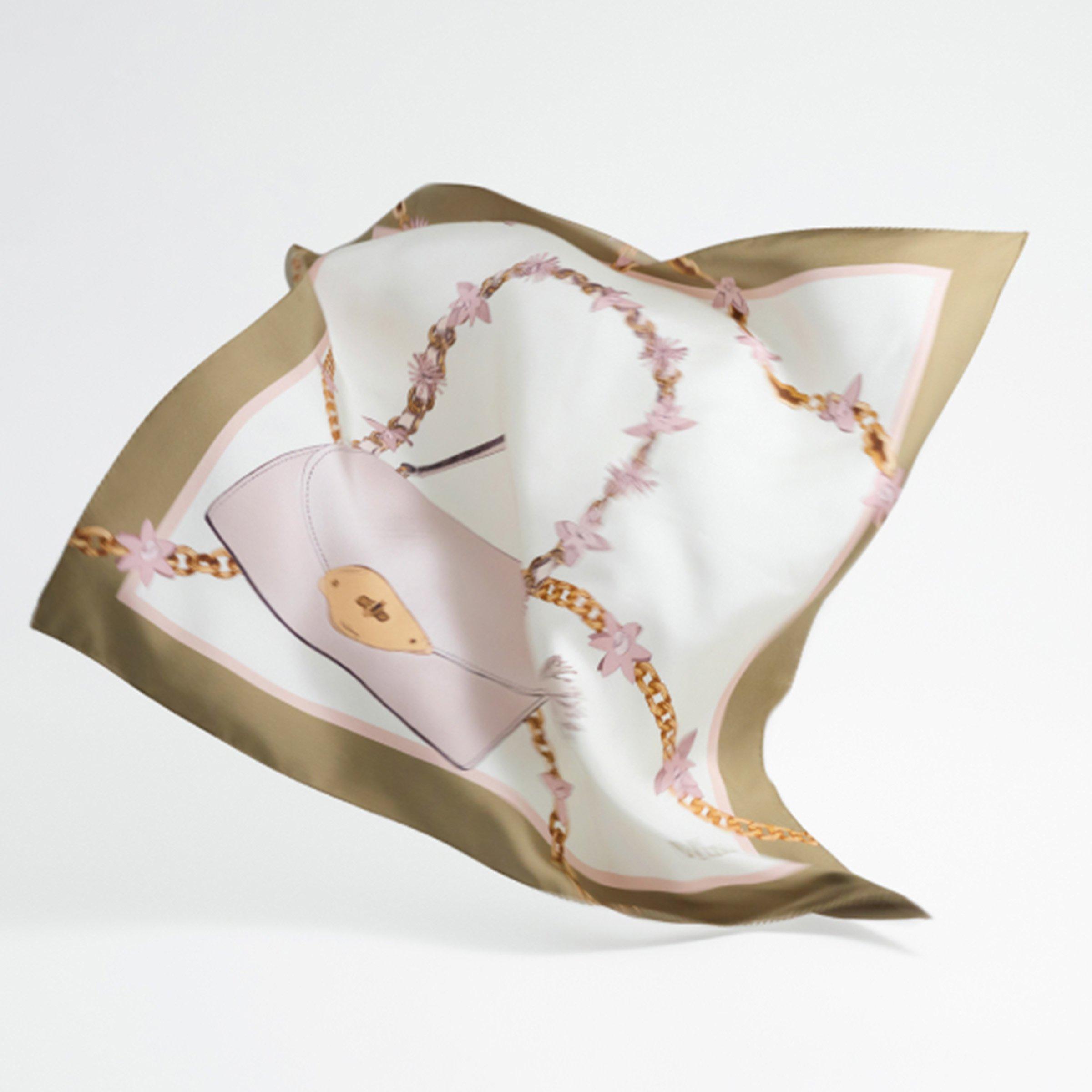 A silk mulberry scarf with a print of a pink handbag and gold chain adorned with pink flowers, set against a white background with olive green and pink borders