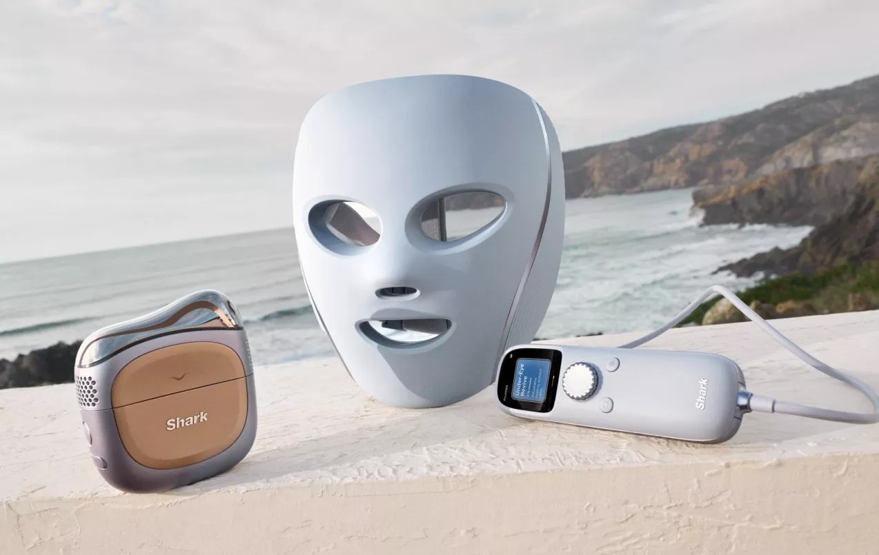 Shark LED face mask and skincare device set on terrace, with coastal sea and cliffs in the background