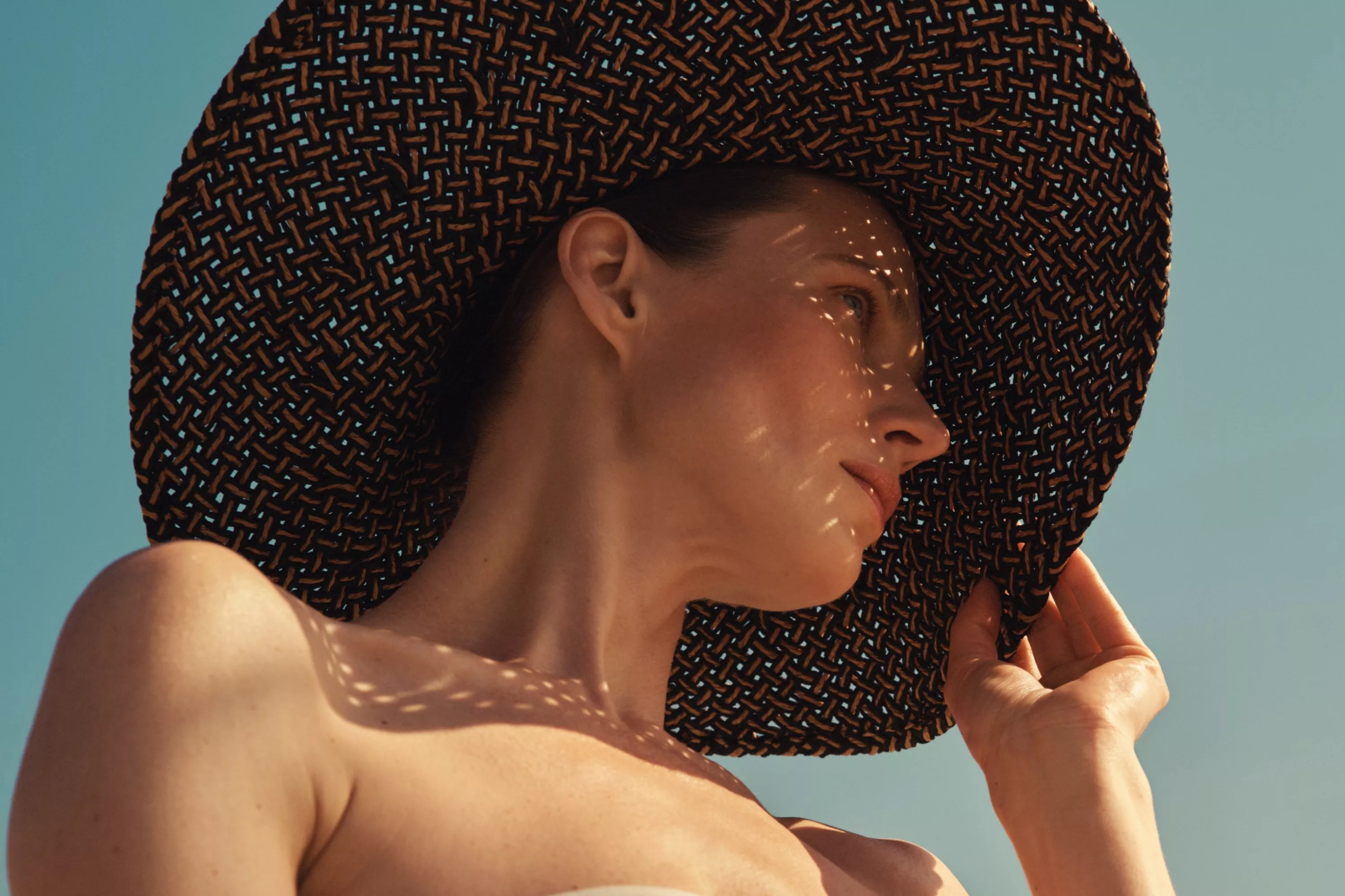 Close-up of woman in woven straw sun hat, sunlit skin and blue sky, summer holiday fashion portrait