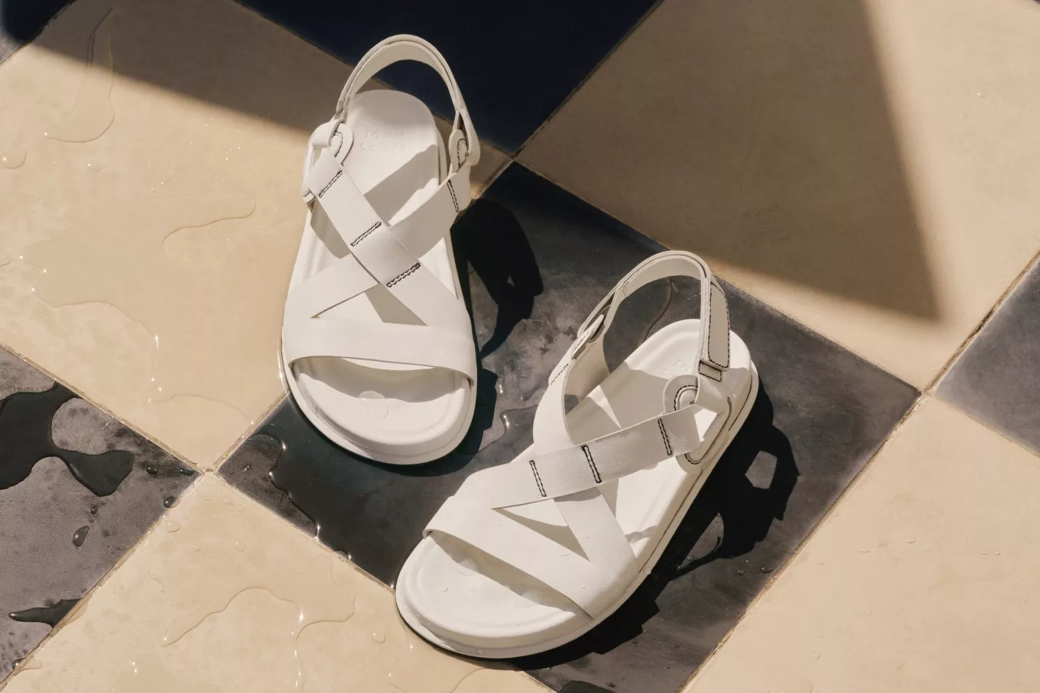White leather strappy sandals on wet tiled floor in sunlight, minimalist summer footwear product photo