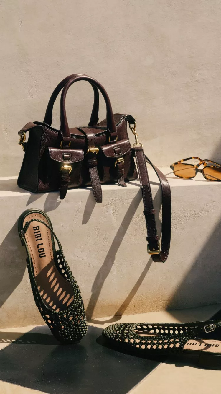 Brown leather satchel handbag with strap, tortoiseshell sunglasses and green woven flats on sunlit steps