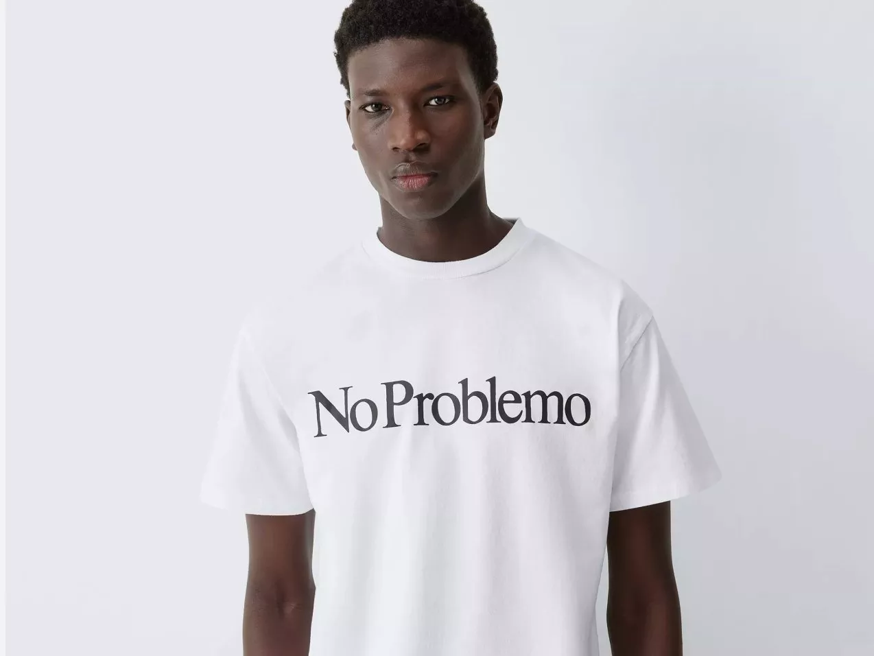 Male model wearing white No Problemo logo T-shirt, front view on studio background, minimalist streetwear style