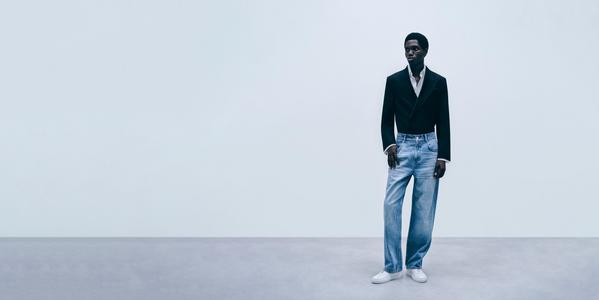 Male fashion model wearing black blazer, white shirt and light blue jeans in minimalist studio setting
