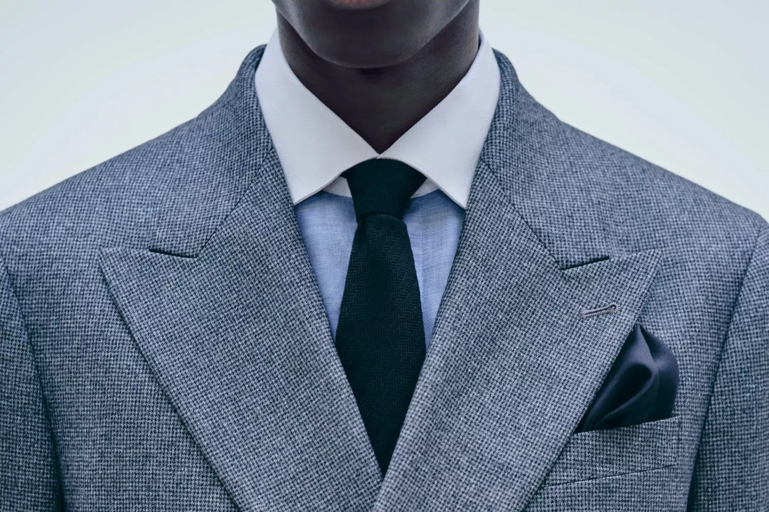 Close-up of a man in a grey tweed suit with white shirt, dark tie and pocket square, smart business attire