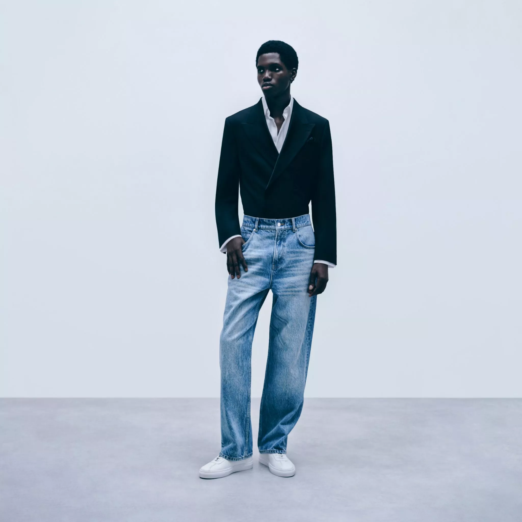 Full-length fashion model in black blazer, white shirt and light blue jeans, minimalist studio style outfit
