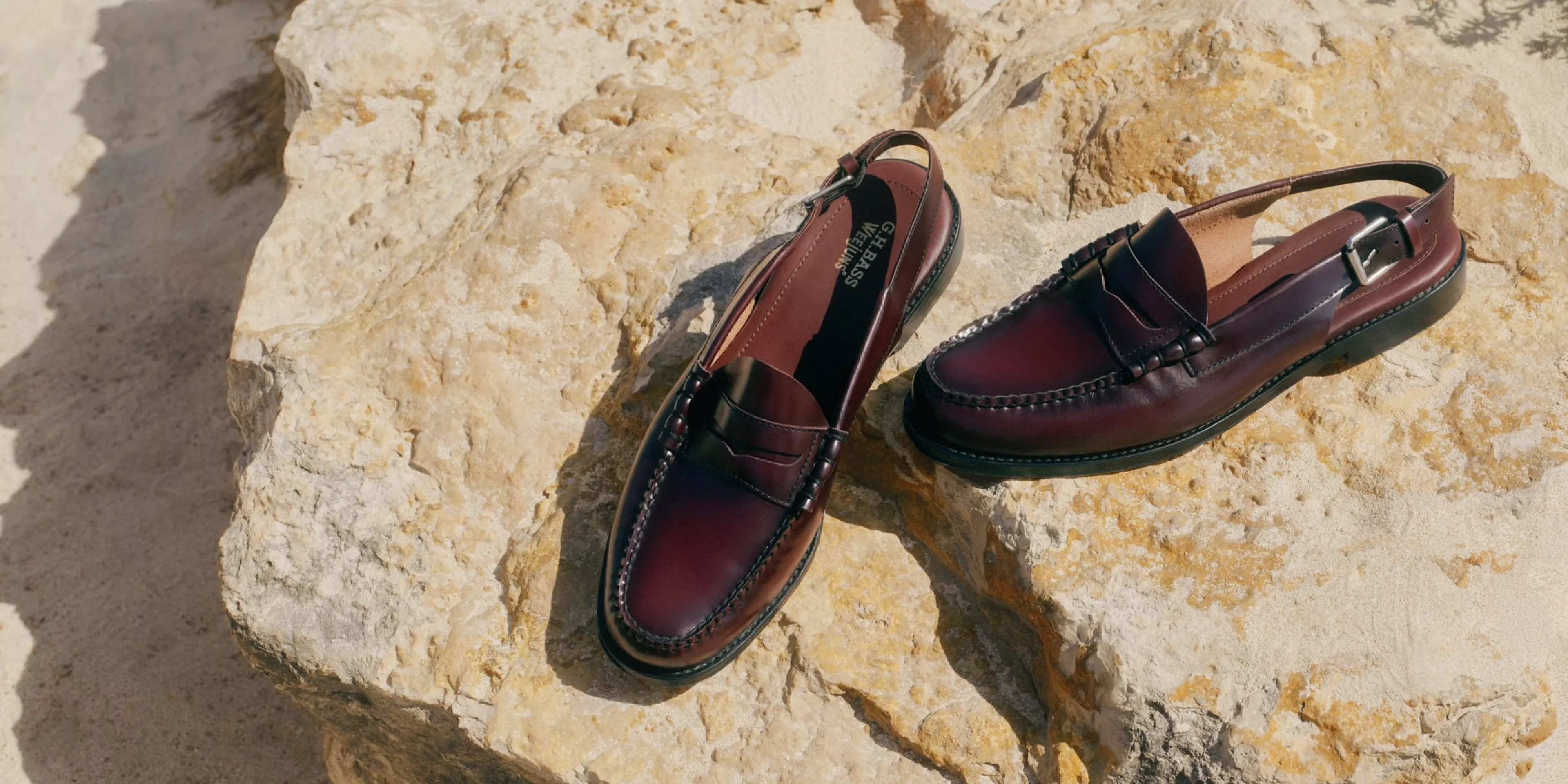 Burgundy leather penny loafers on sunlit rock, classic men’s smart shoes with stitched detailing and strap back