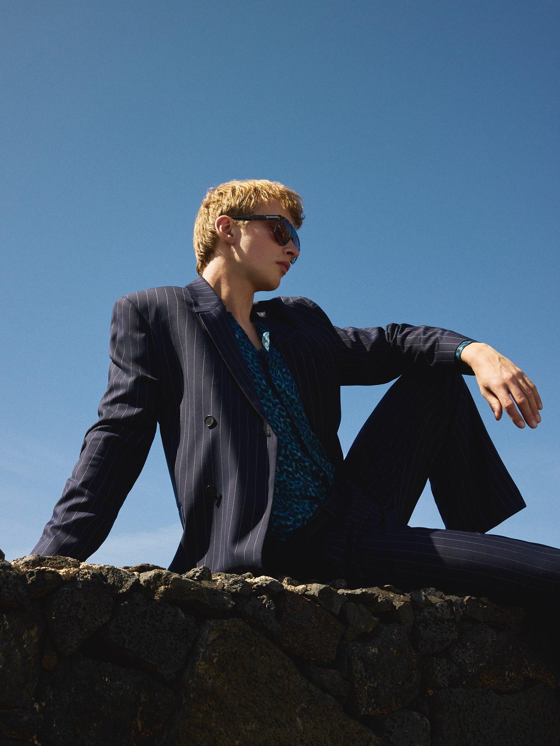 Man in pinstripe dark suit jacket and trousers sitting on rocky ledge
