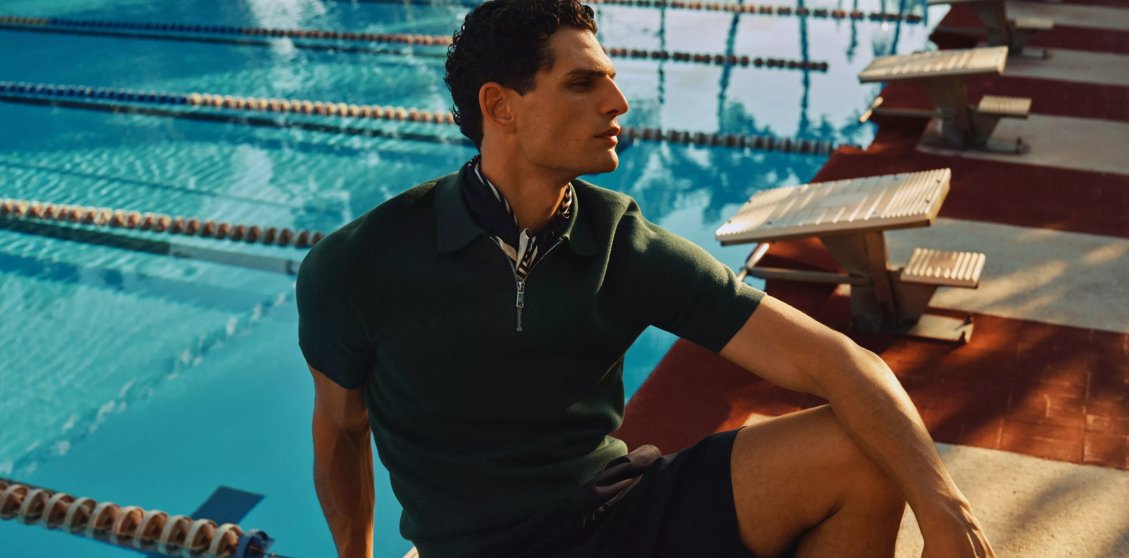 man sitting on the ede of a swimming pool wearing a polo shirt