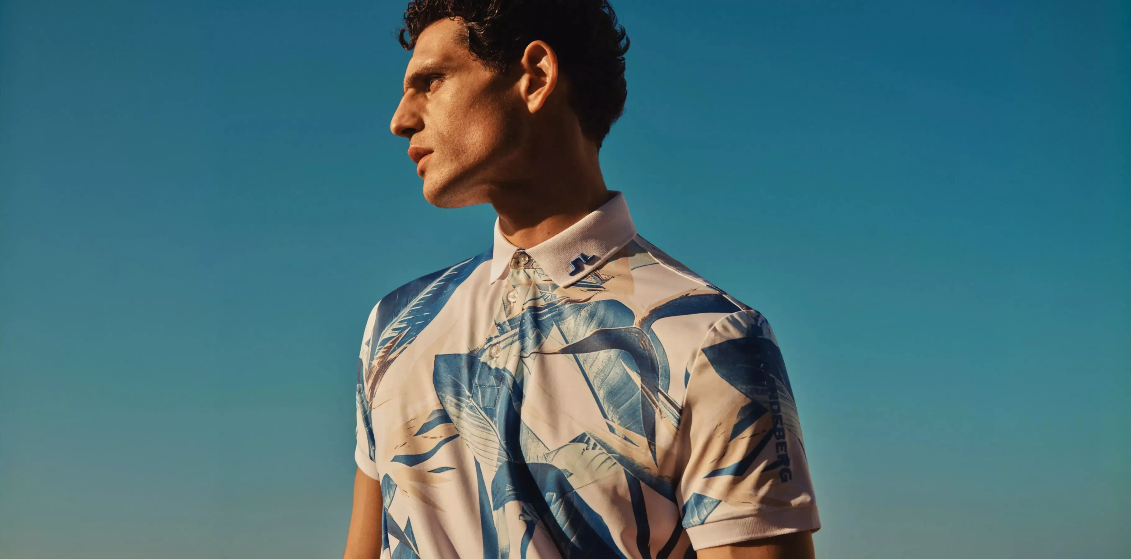 mens wearing a bold blue and white patterned polo with clear blue sky behind him