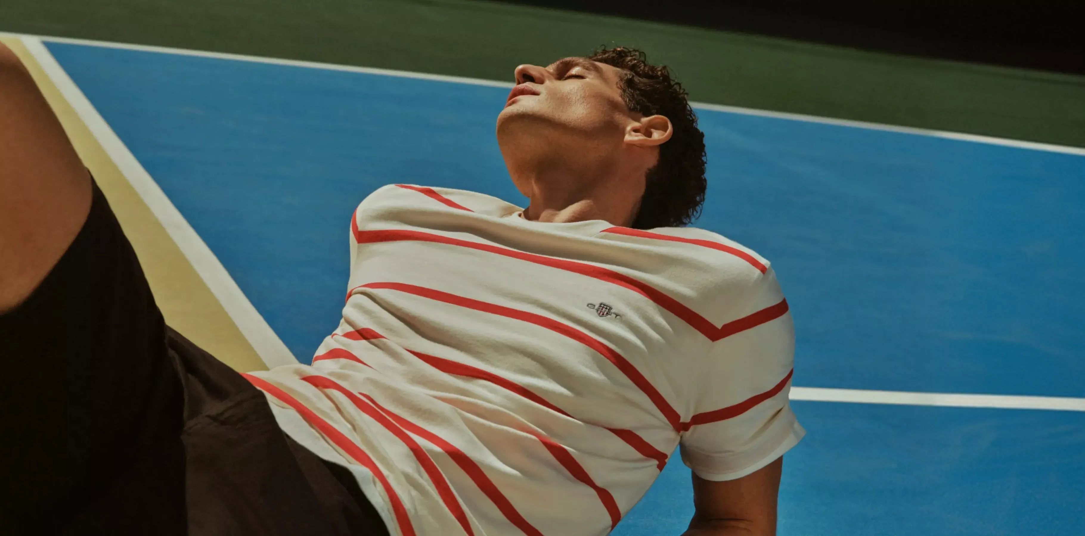 a man wearing a t-shirt lying on a tennis court
