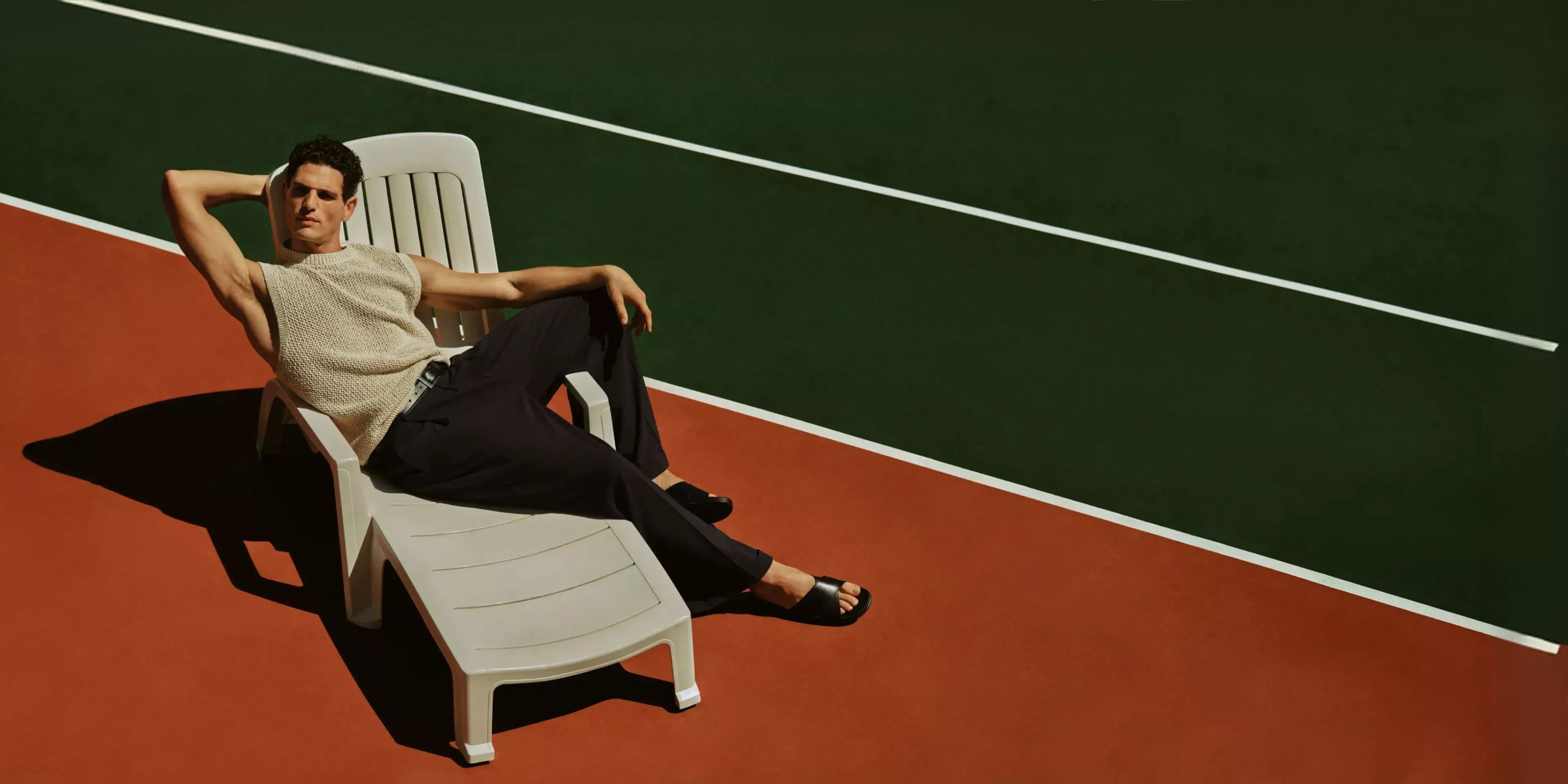 man in smart clothes sitting on a lounger on a tennis court