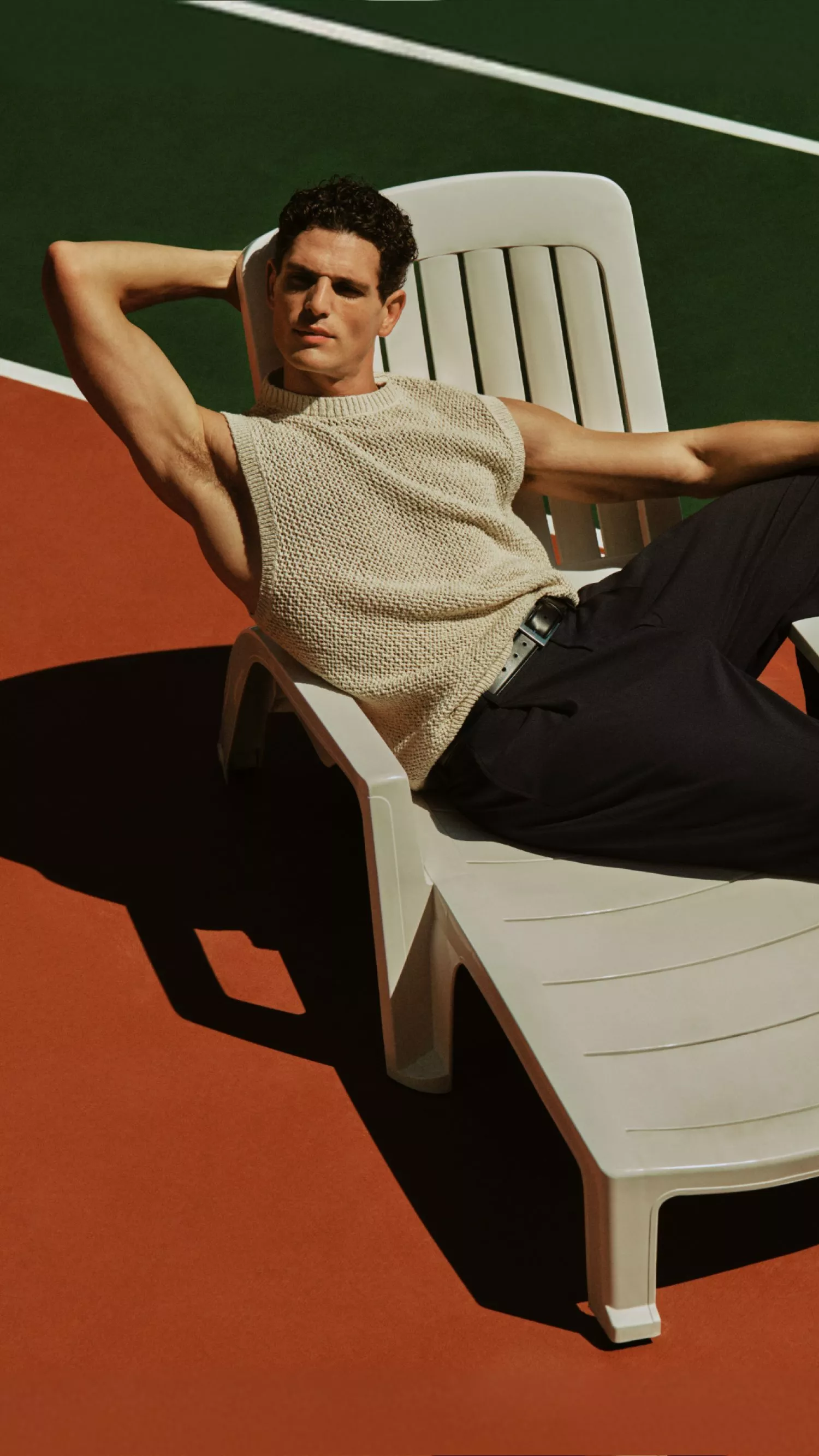 man in smart clothes sitting on a lounger on a tennis court
