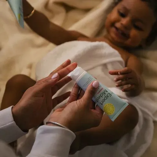 Parent applying gentle baby moisturiser while toddler lies smiling on bed, natural skincare routine at home