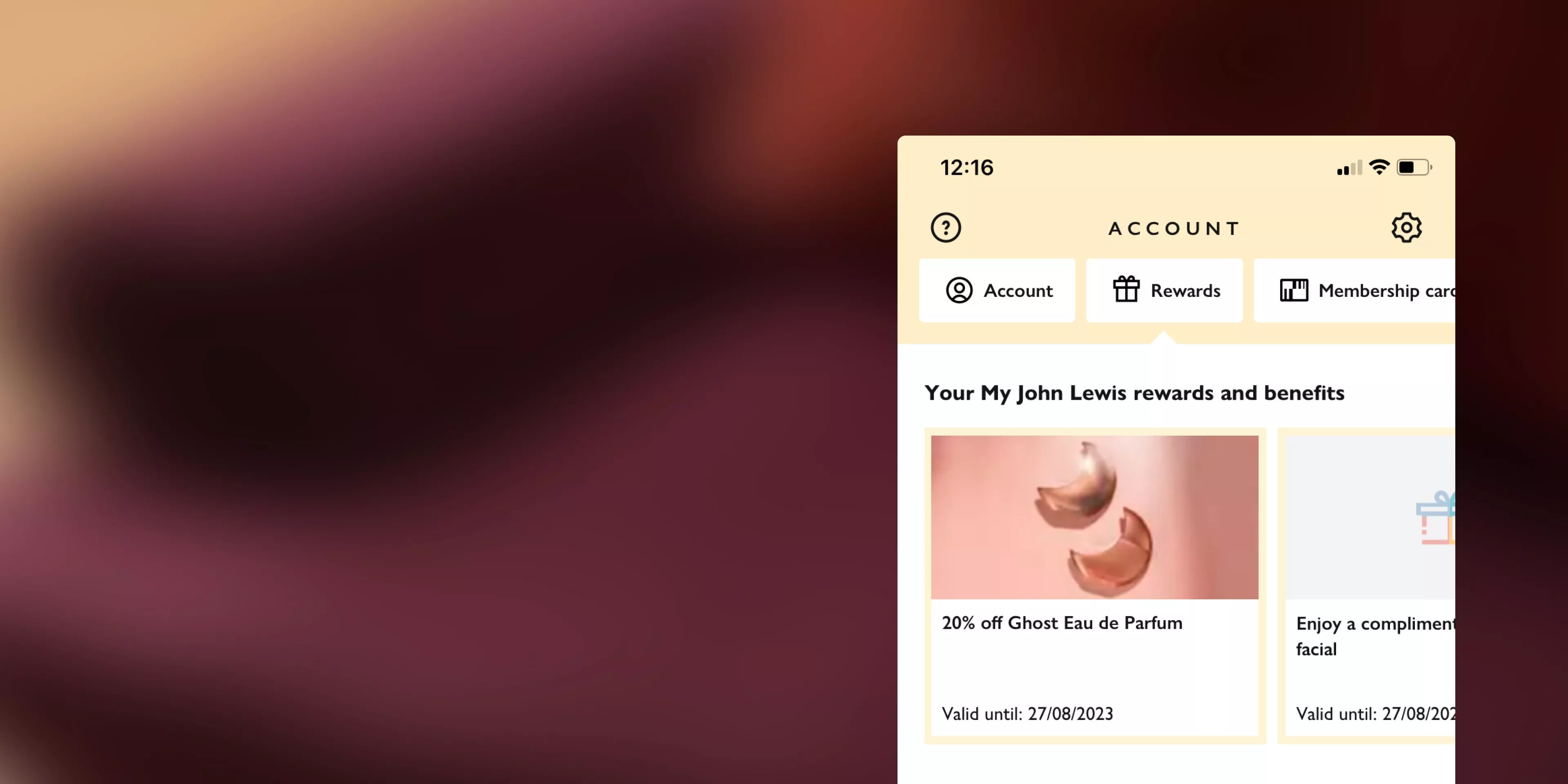 Abstract, blurred background of dark maroon, brown, and a light peach tone, with a mobile app screen showing account and rewards.