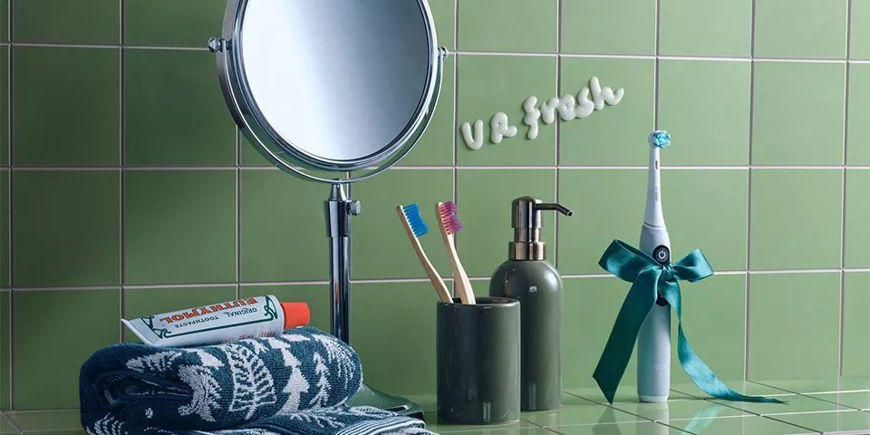 Round pedestal mirror next to a toothbrush holder, soap dispenser and towel
