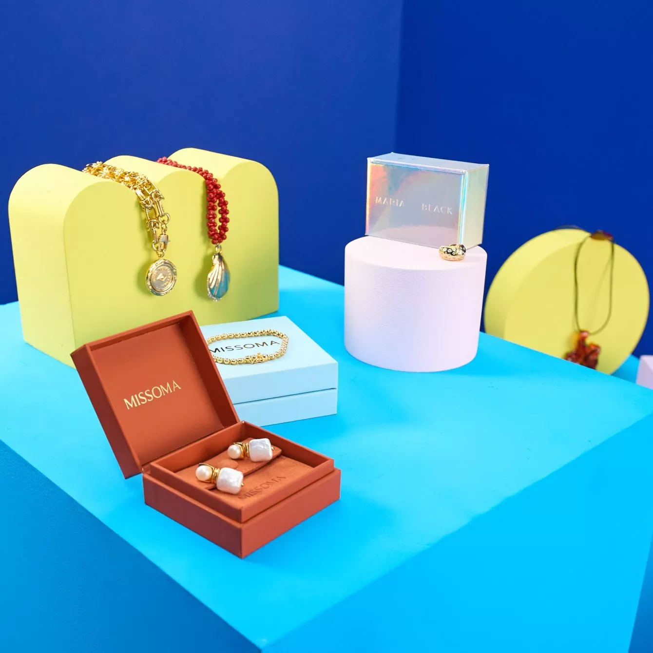MISSOMA jewellery display with gold necklaces, pearl earrings and gift boxes on a bright blue studio set