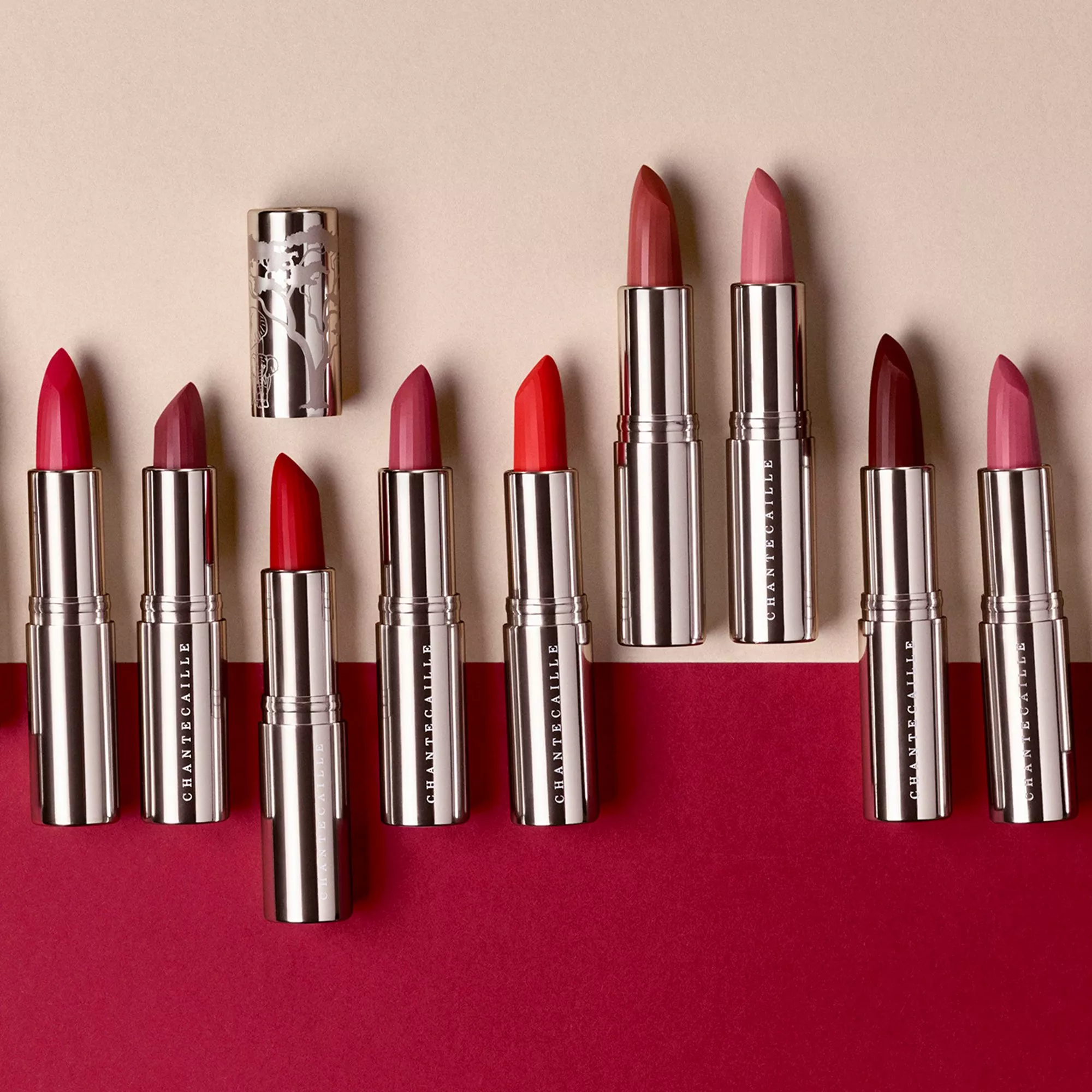Assorted luxury lipsticks in silver tubes, red and pink shades arranged on a textured crimson background