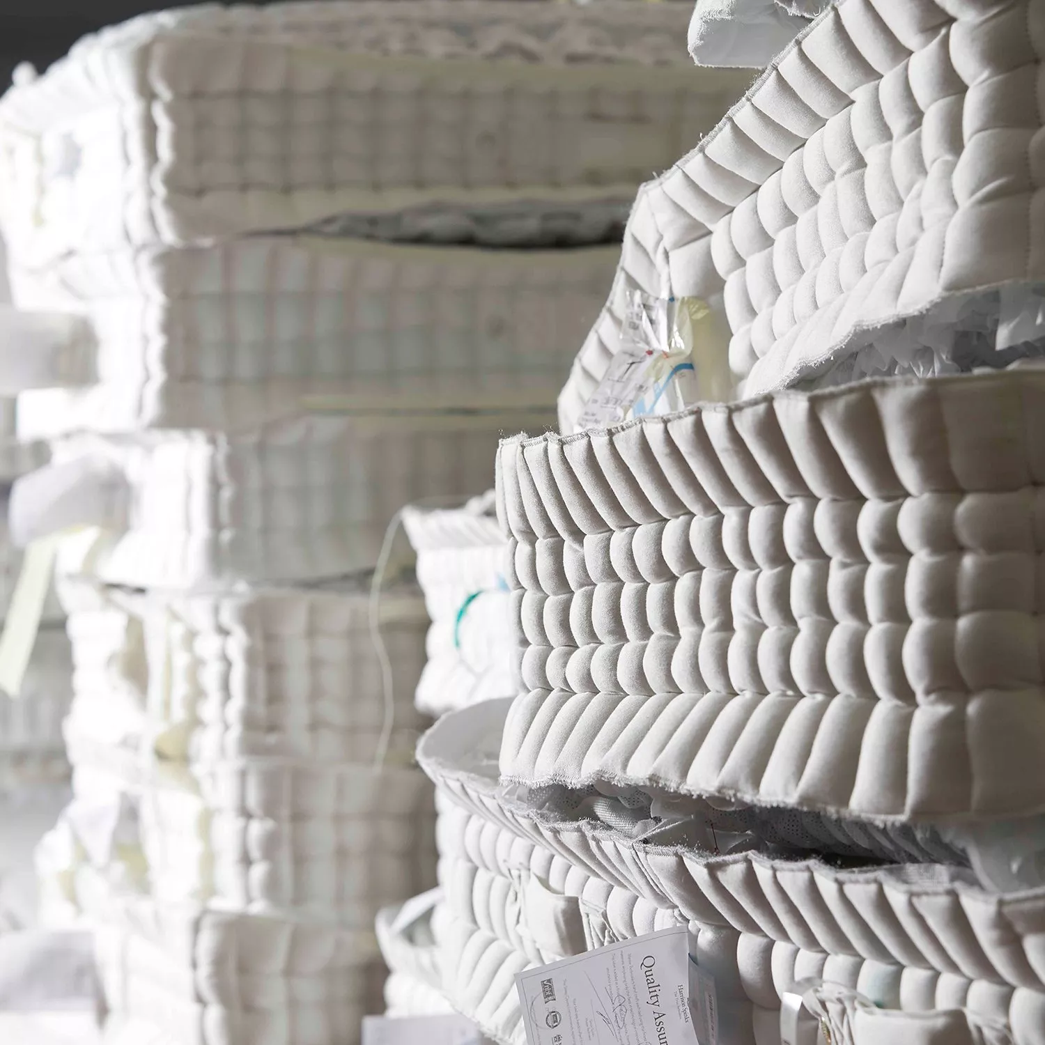 Stacked pocket sprung mattress layers in factory, showing quilted upholstery and mattress manufacturing process