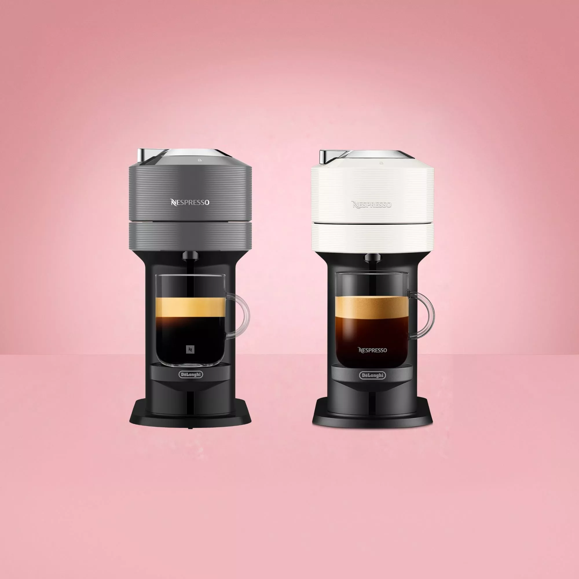 Two Nespresso Vertuo Pop coffee machines by De'Longhi—one in grey and one in white—side by side on a soft pink background, each with a filled glass mug of coffee resting on its drip tray.