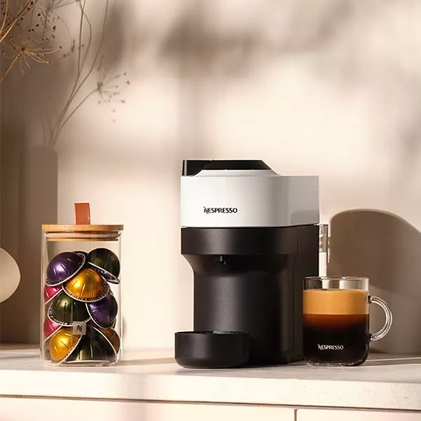 Black and white Vertuo Pop machine with capsules in a jar next to it and a freshly made coffee