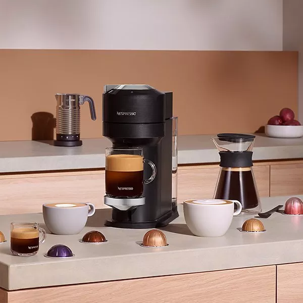 Black Vertuo Next machine with a freshly made coffee and accessories scattered around it 