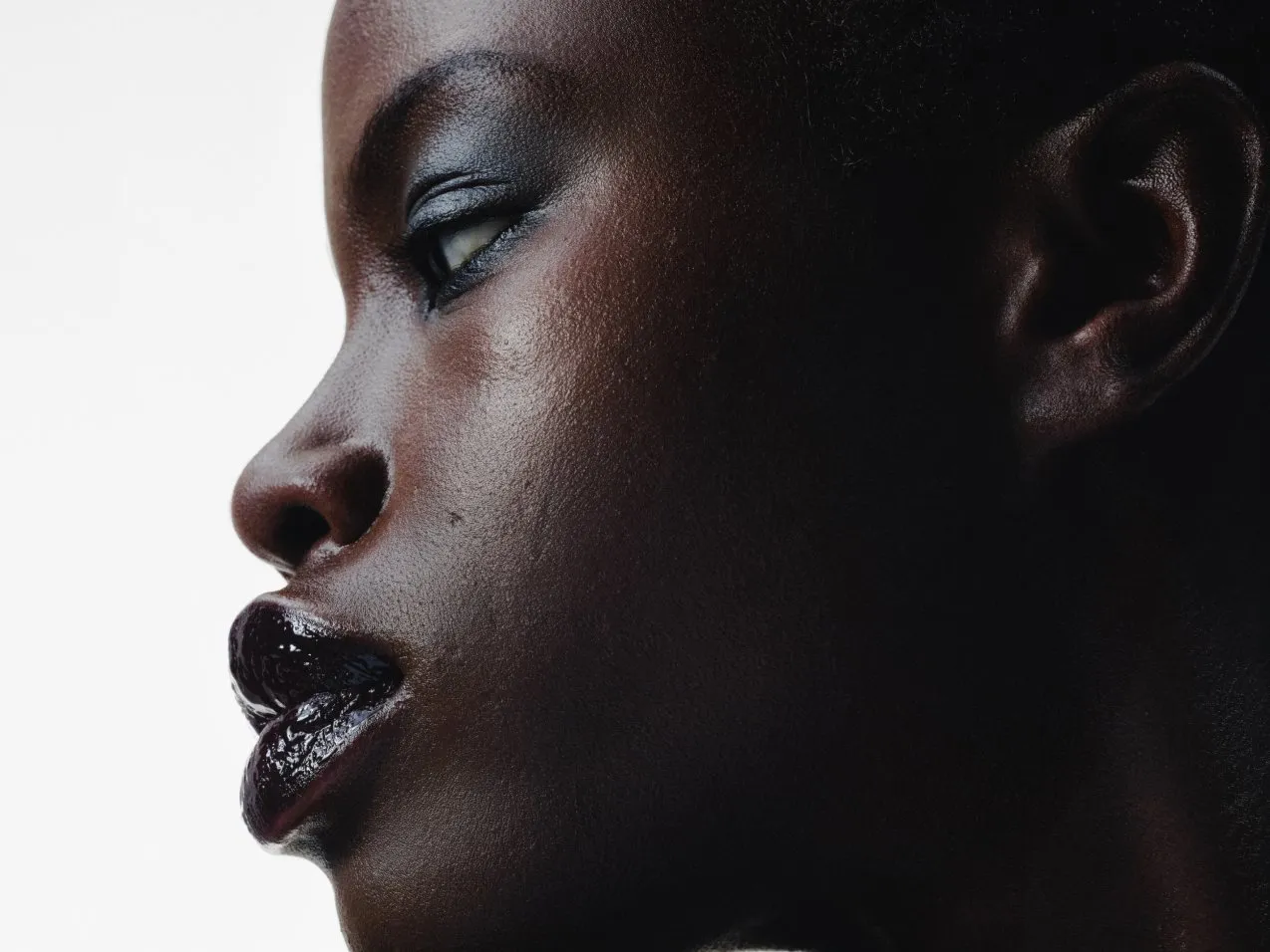Close-up side profile portrait with dramatic lighting, glossy lips and smoky eye make-up on white background