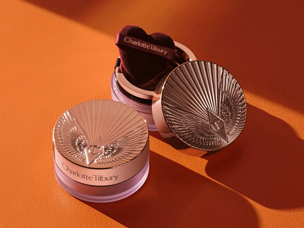 Charlotte Tilbury Airbrush Flawless Finish powder compact and puff on orange background, rose-gold case close-up