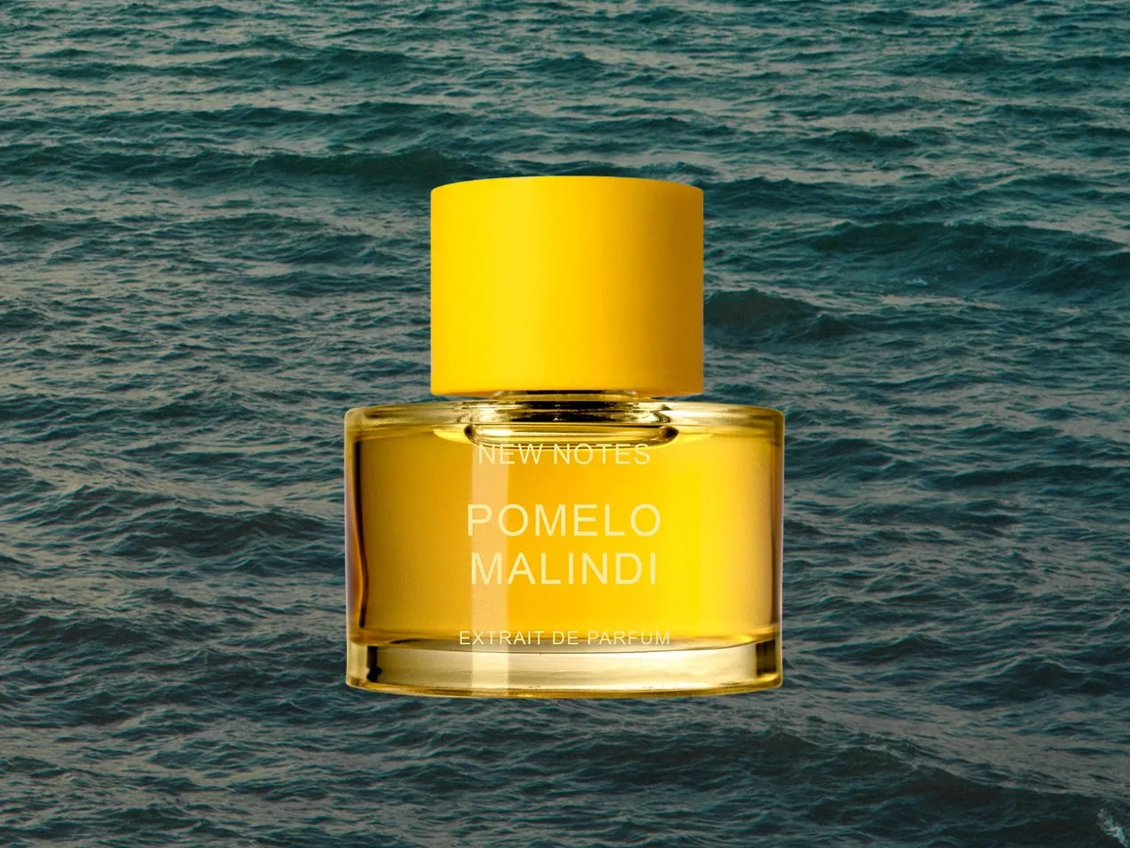 New Notes Pomelo Malindi extrait de parfum bottle with yellow cap, centred against textured ocean water backdrop