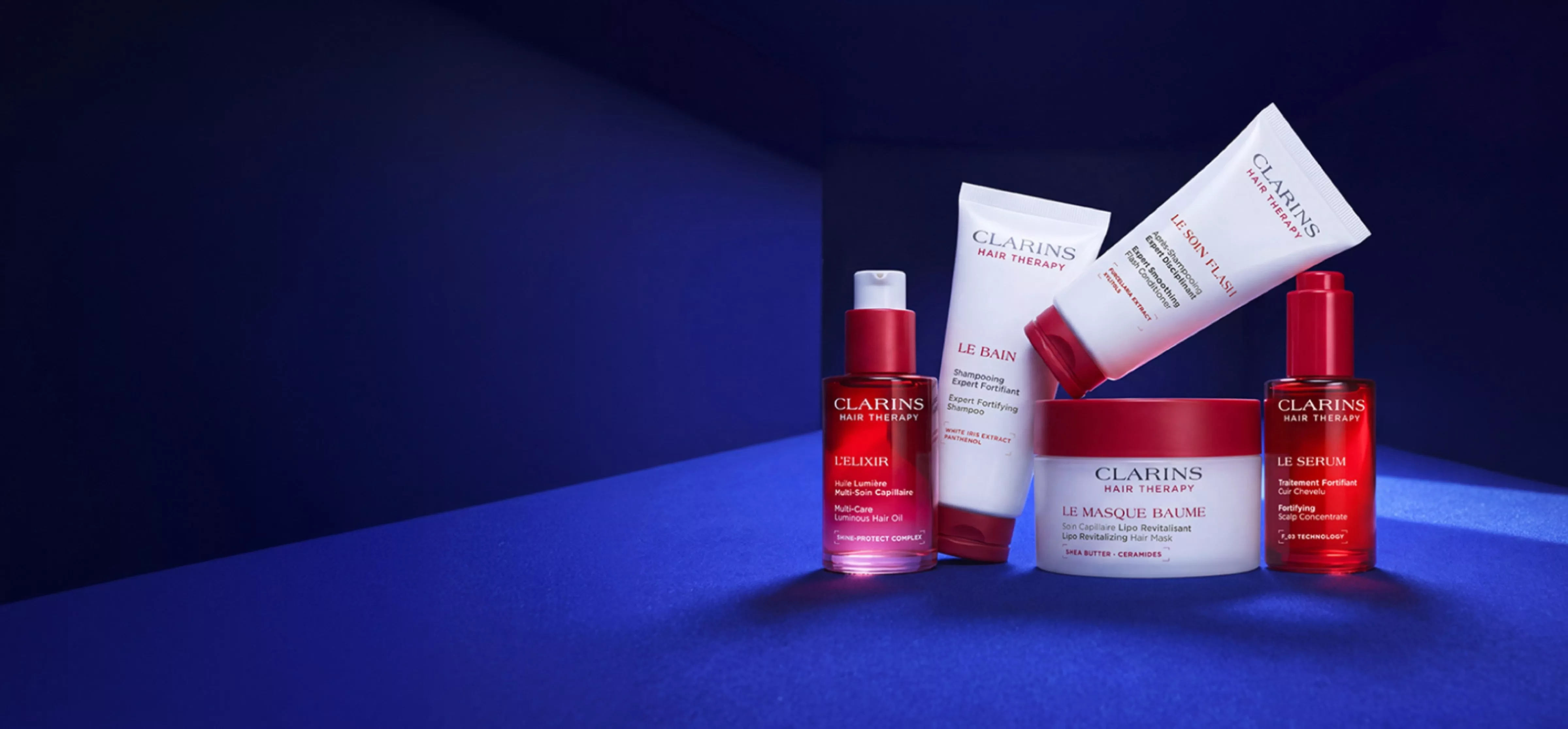 Clarins Hair Therapy range on blue backdrop: shampoo, scalp conditioner, oil elixir, mask and serum products